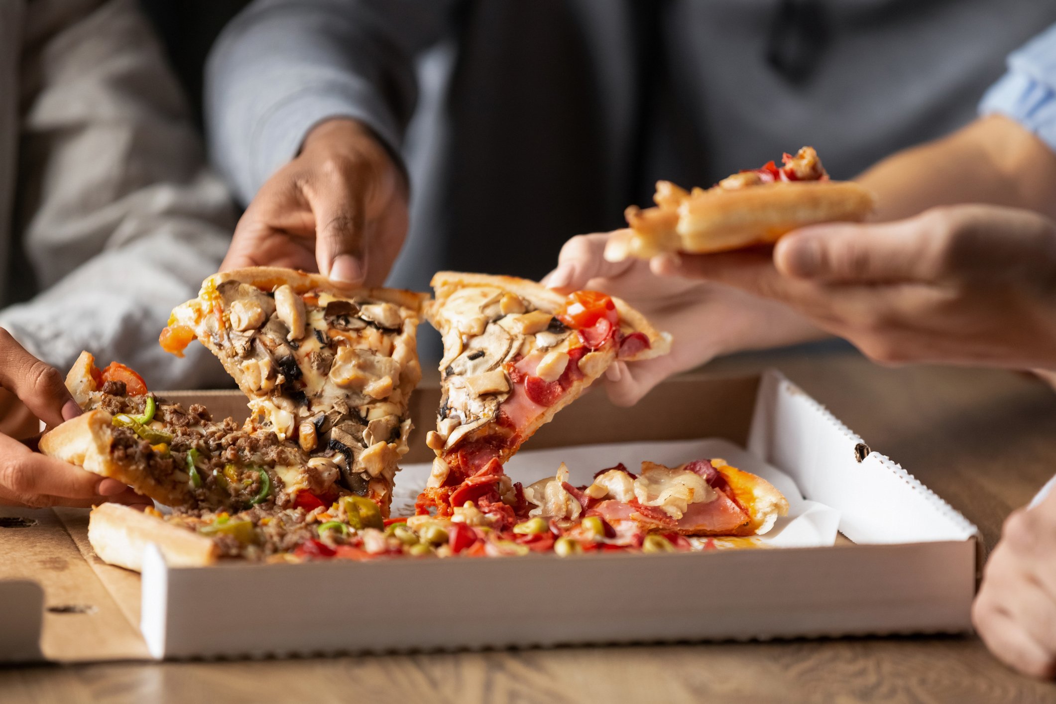 Close up of multiethnic young people gather in pizzeria together grabbing slices of pizza