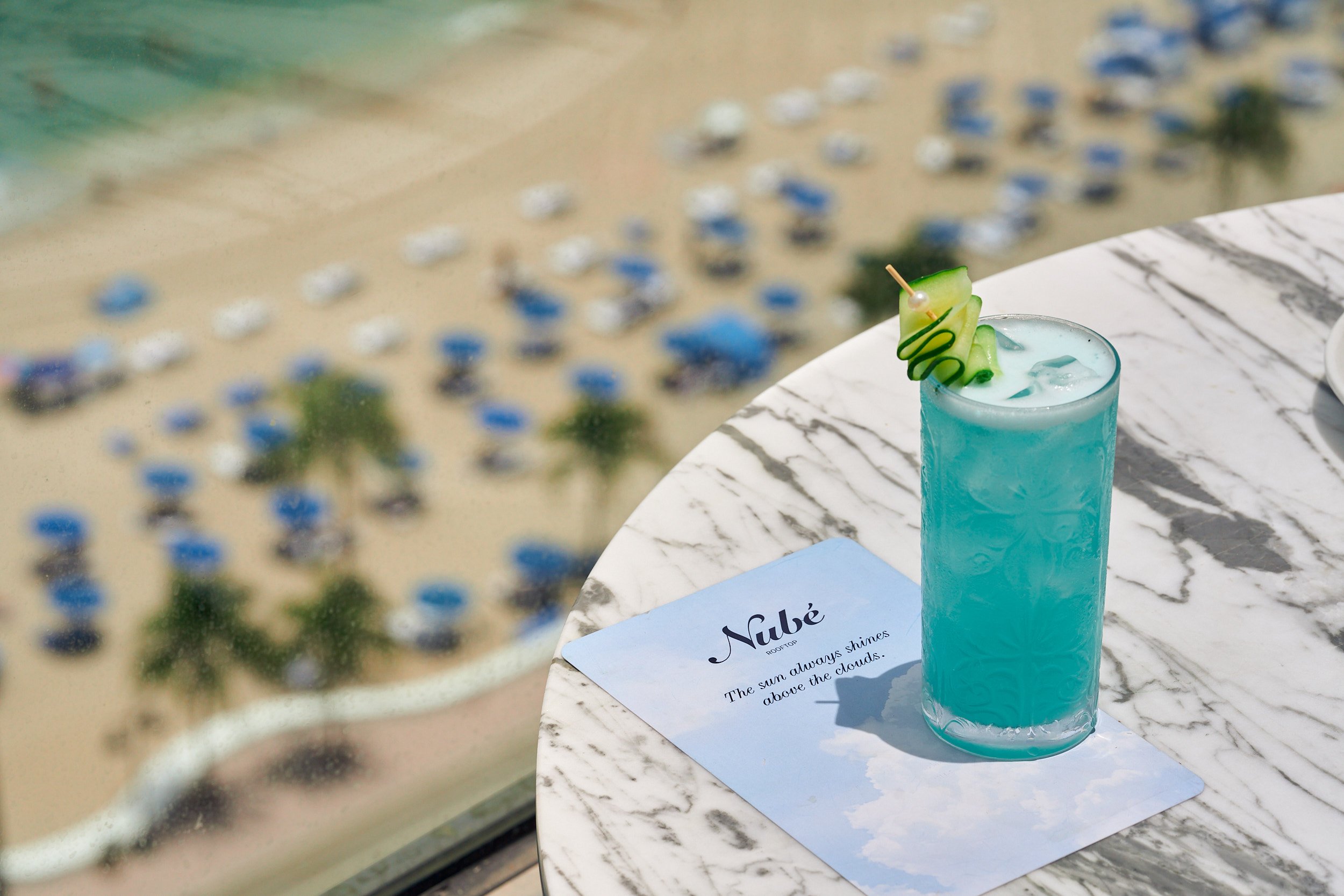 a light blue cocktail with cucumber garnish sits upon the nube menu