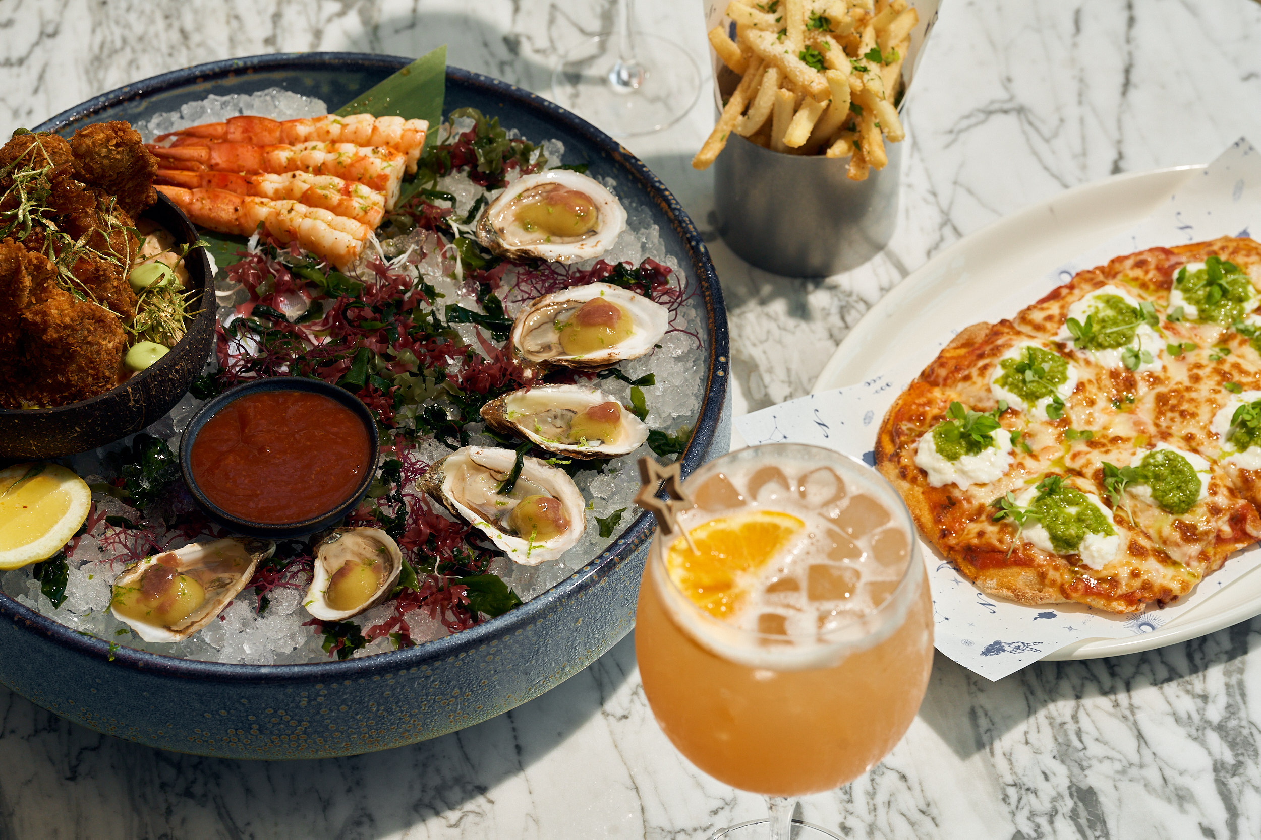 a seafood platter, basket of fries and pizza upon a marble table
