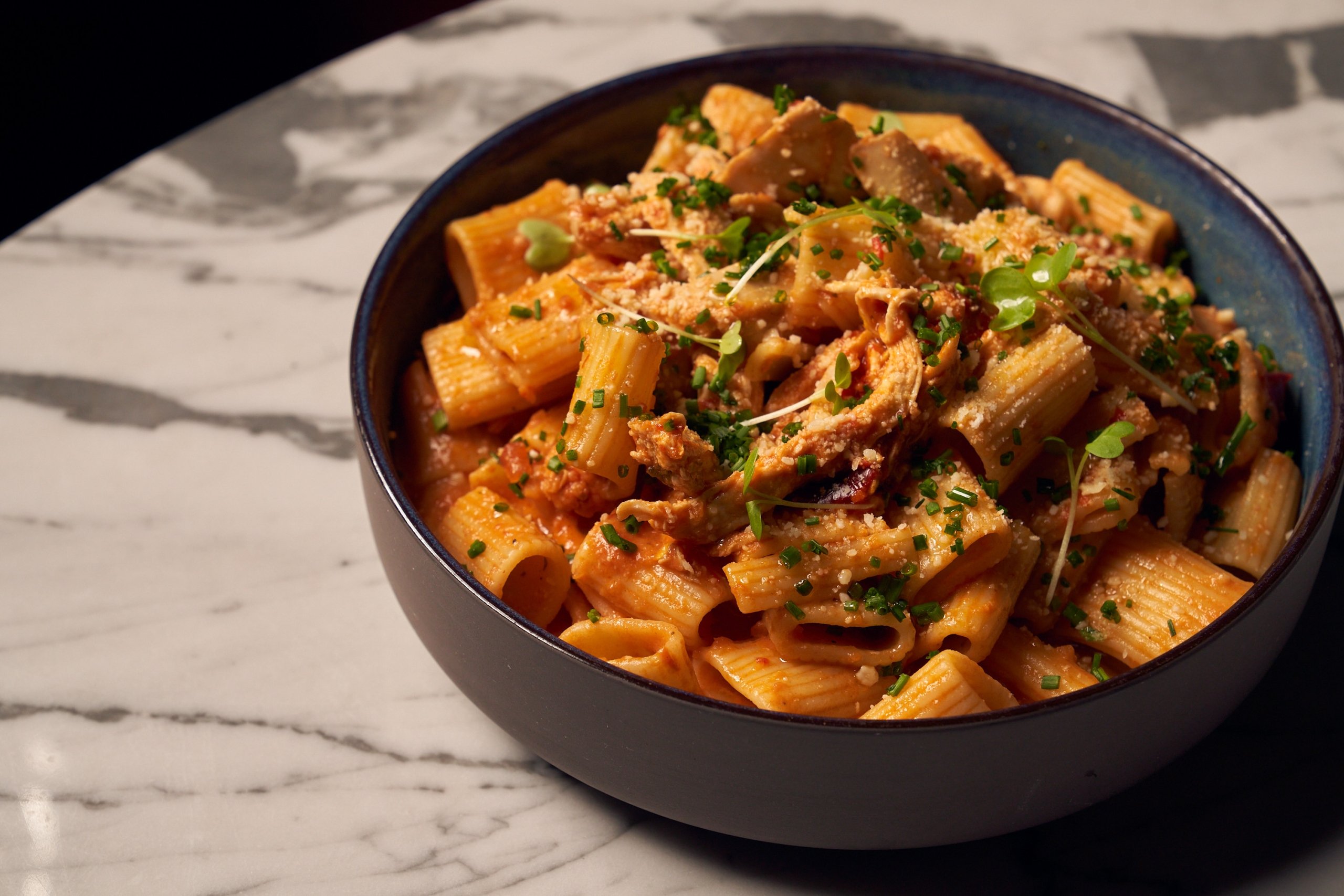 a pasta dish in a black bowl upon a marble table