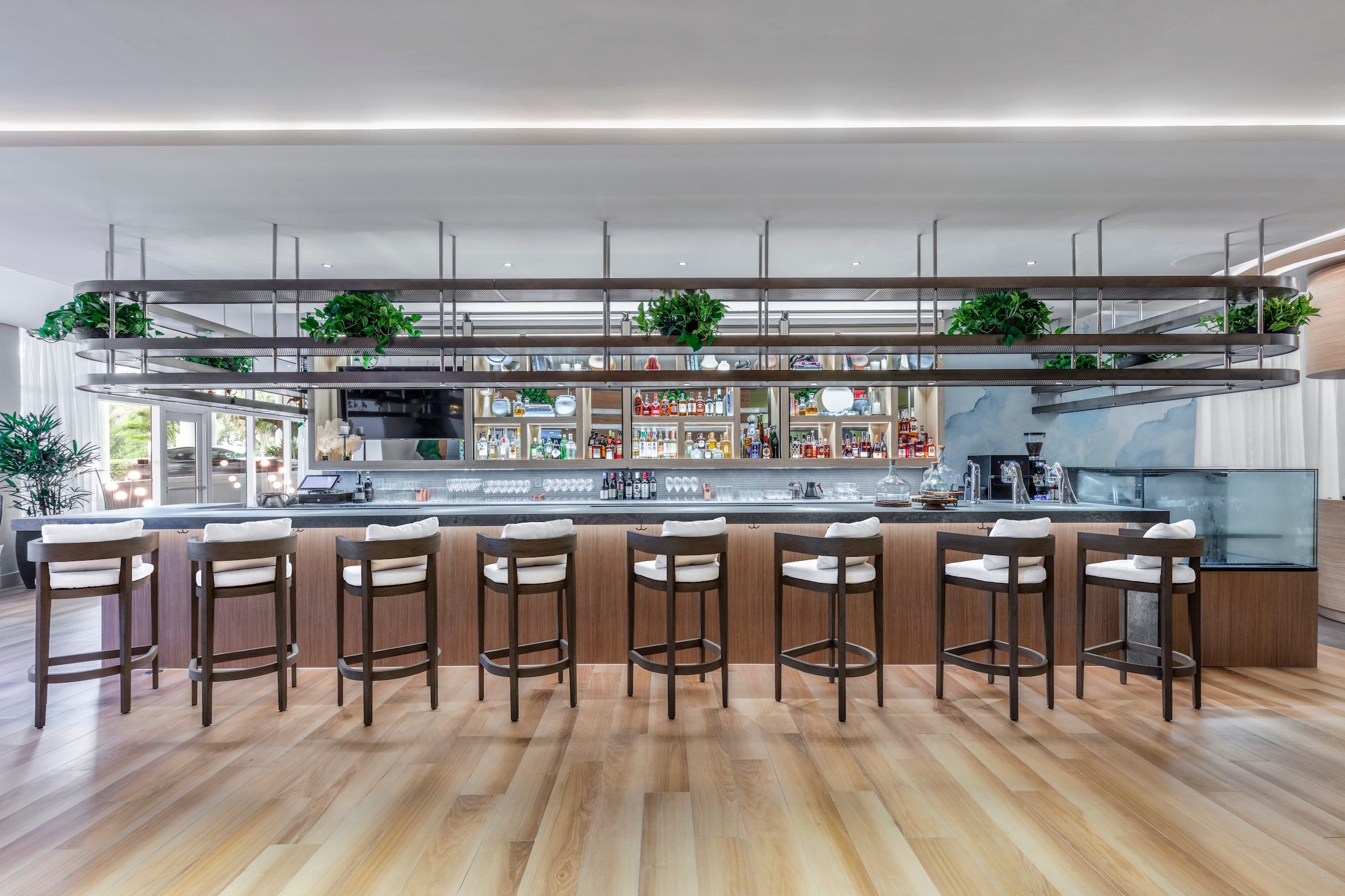 the Barto bar with wood chair and white cushions with various liquor bottles in the background