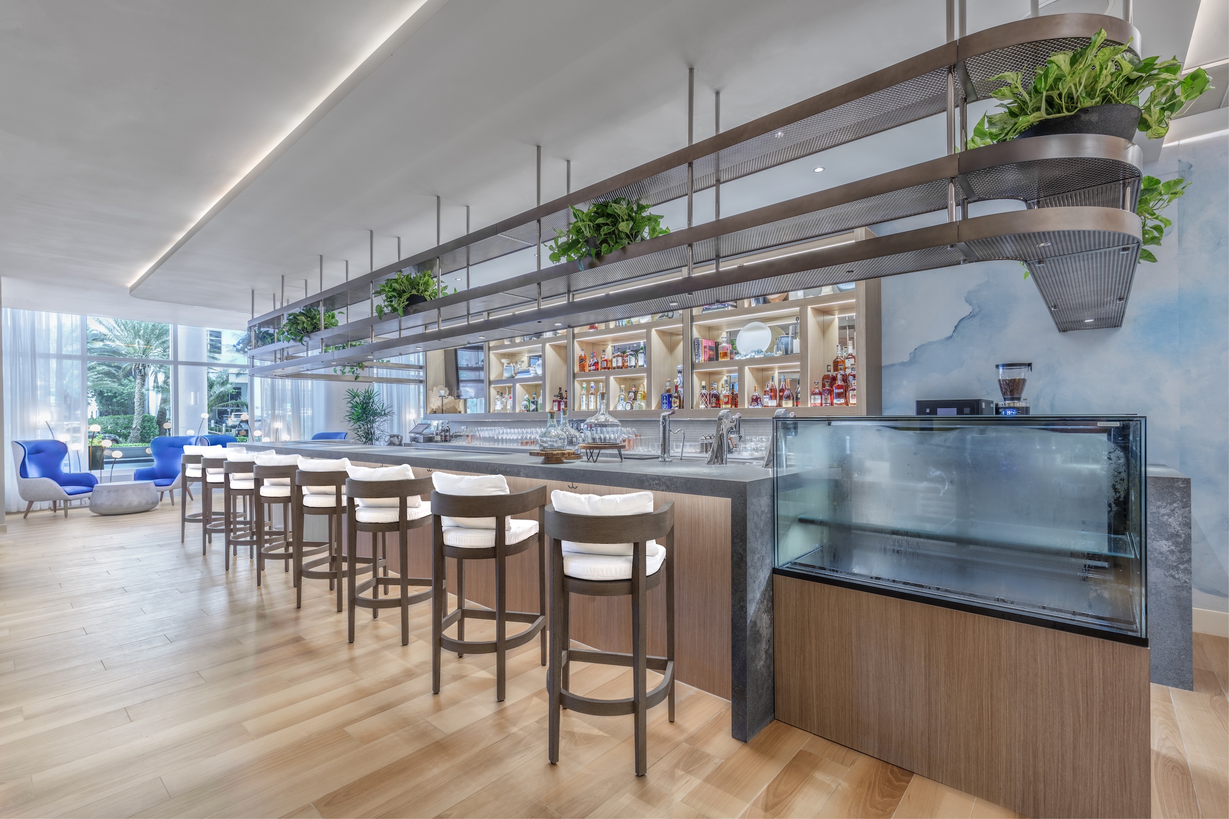 the Barto bar with wood chair and white cushions with various liquor bottles in the background