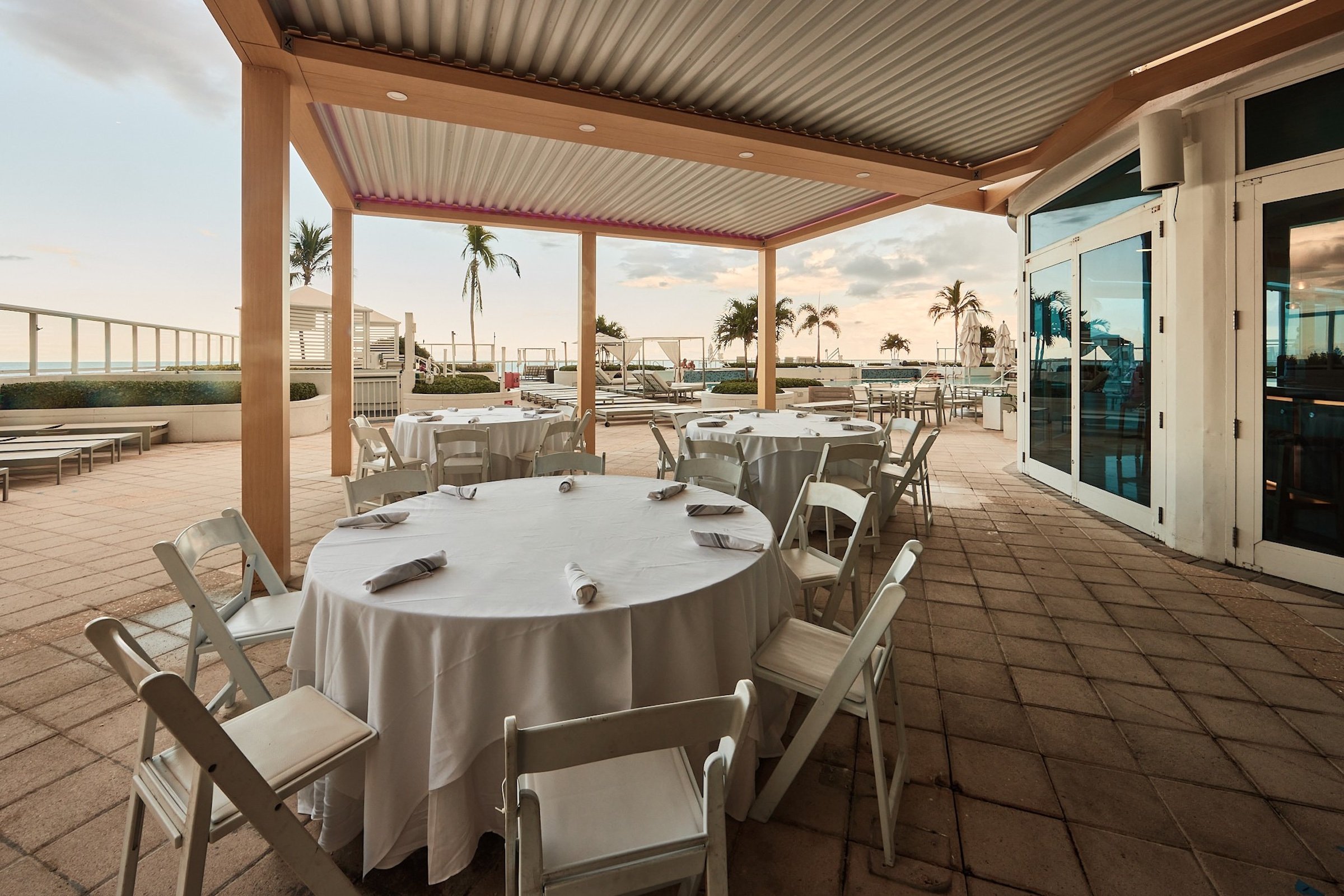 A beachfront terrace with round banquet tables topped with white linens