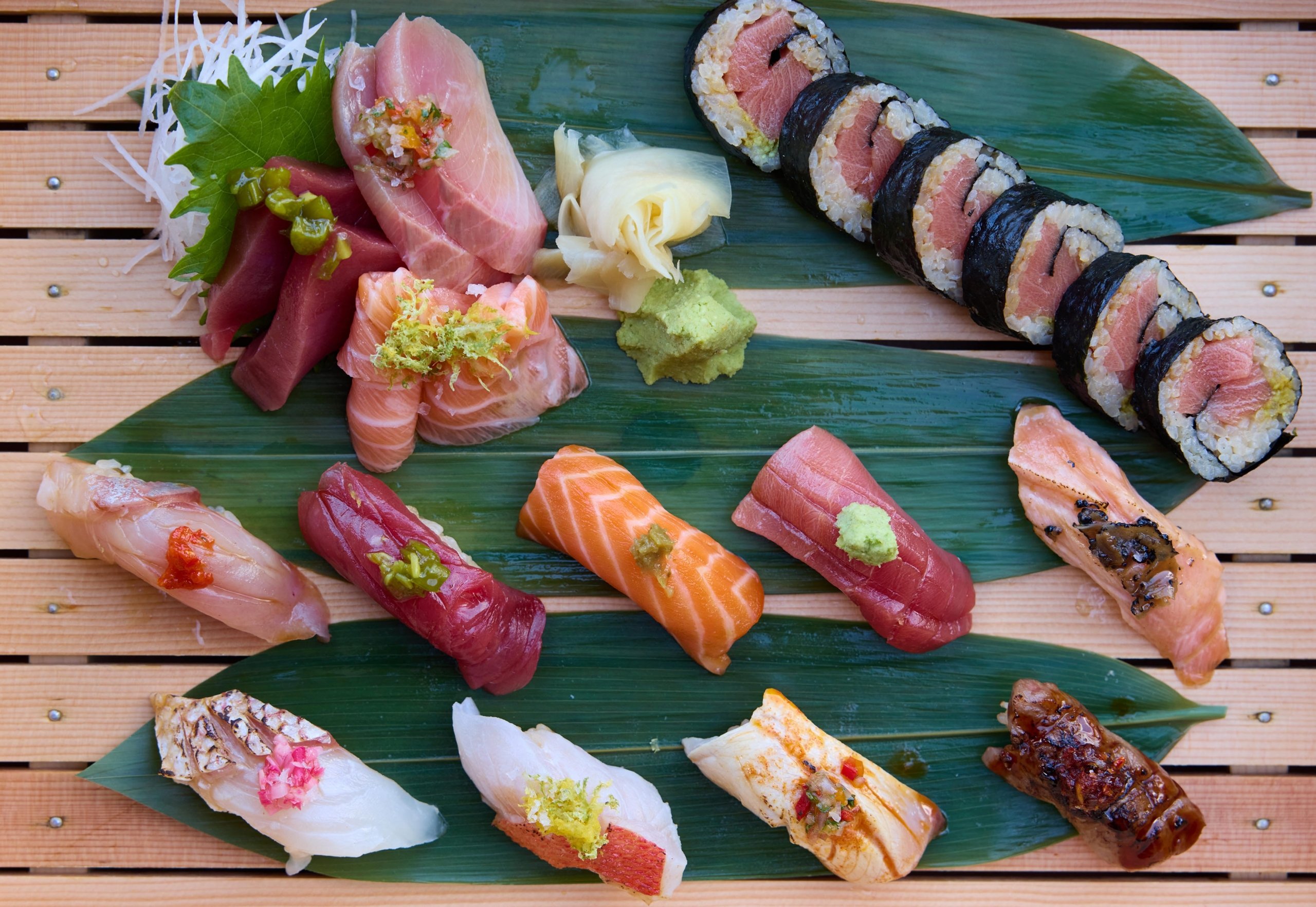 Assorted sushi, displayed on green leaves, sitting on a wood table