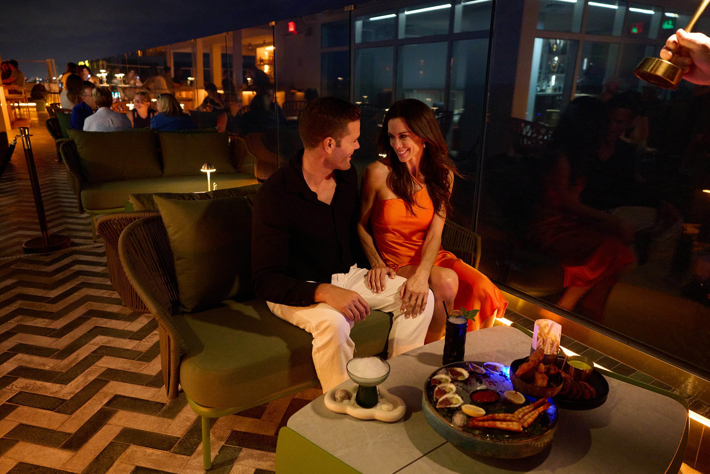 A couple dining on shared plates, on a hip rooftop patio
