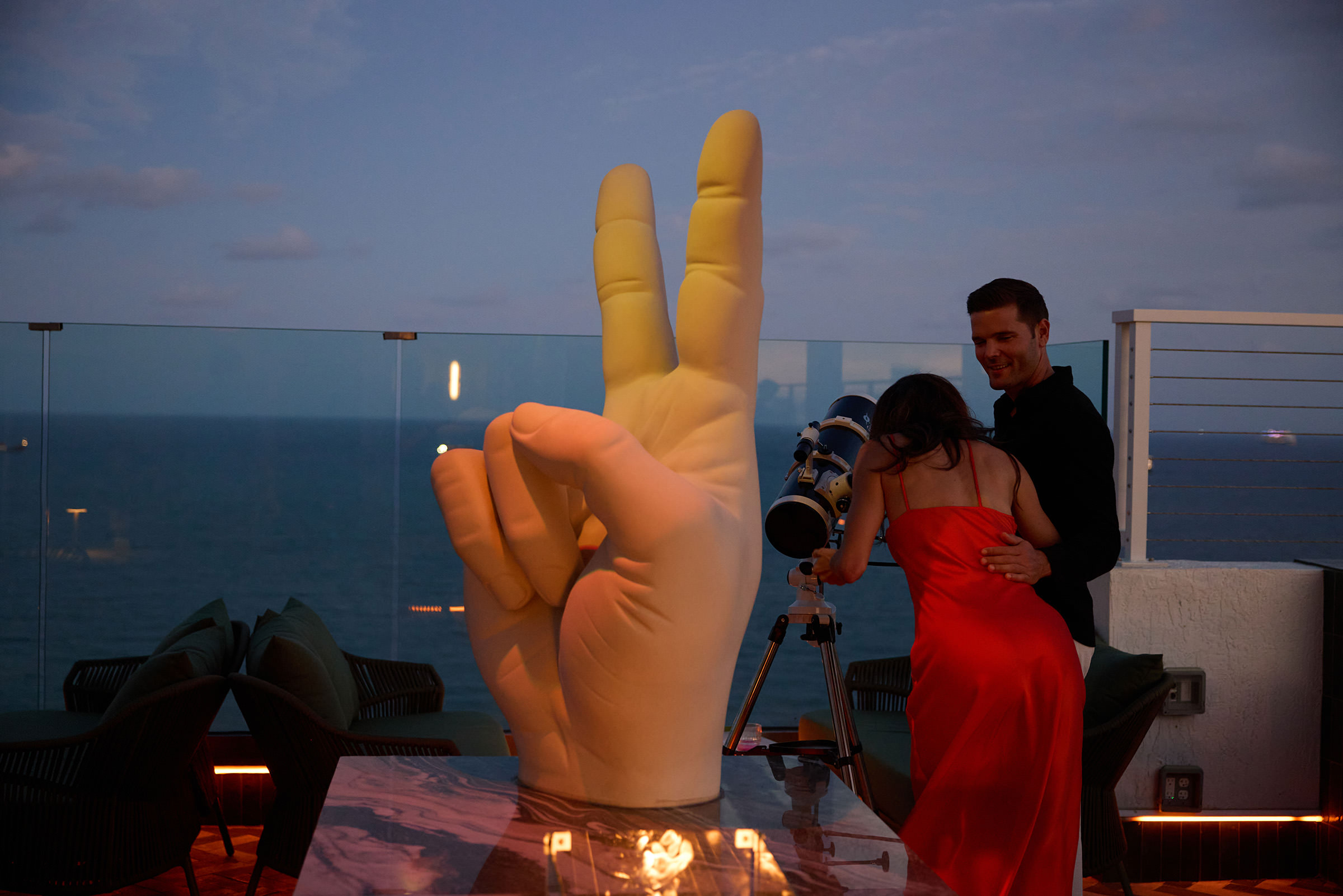 A couple looking through a telescope at dusk on a rooftop patio