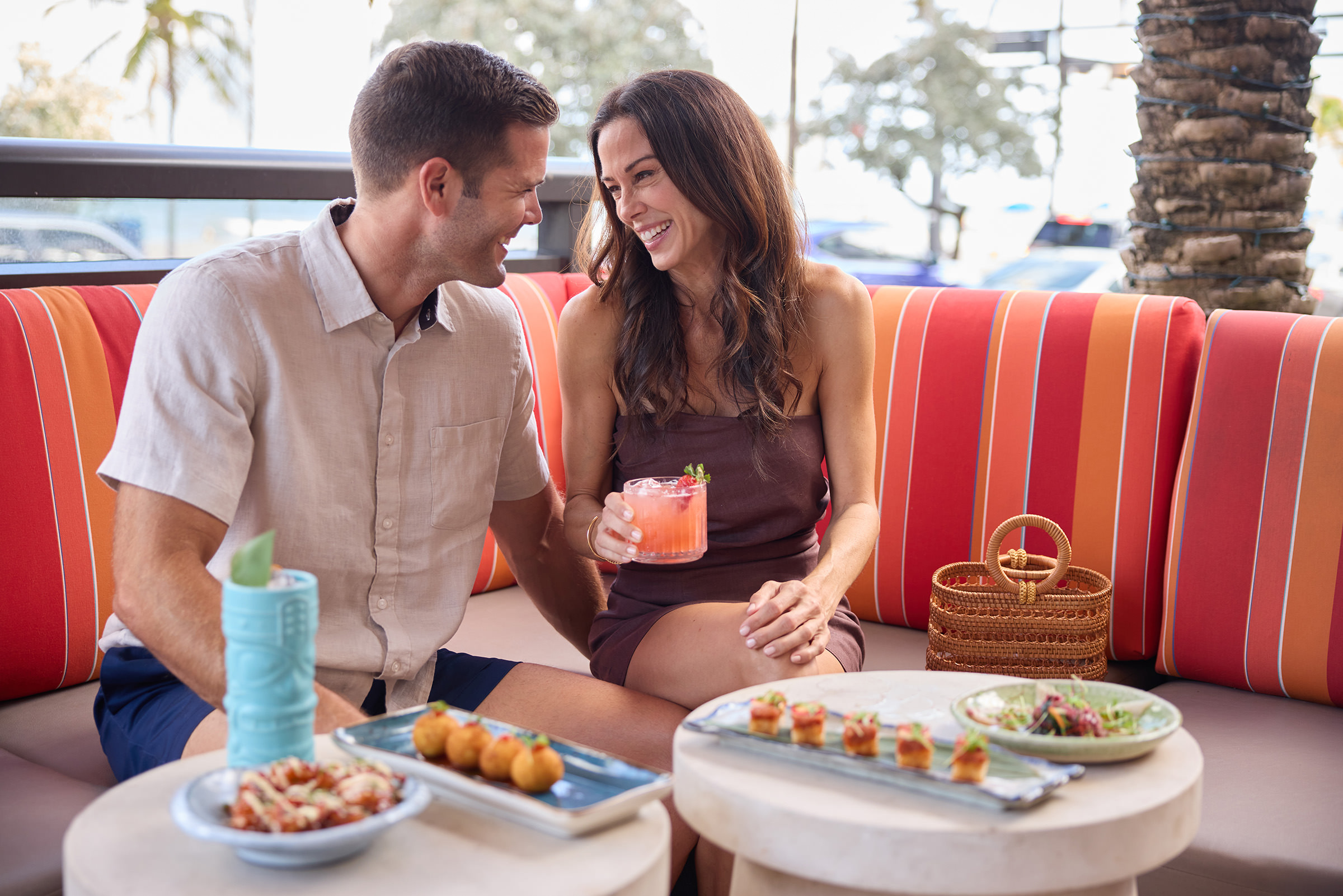 A couple enjoying drinks in a padded booth on an outdoor patio