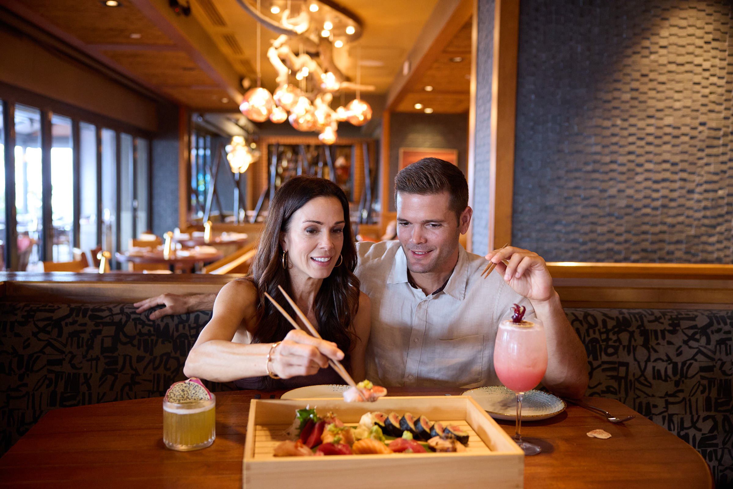 A couple seated in a booth, sharing sushi