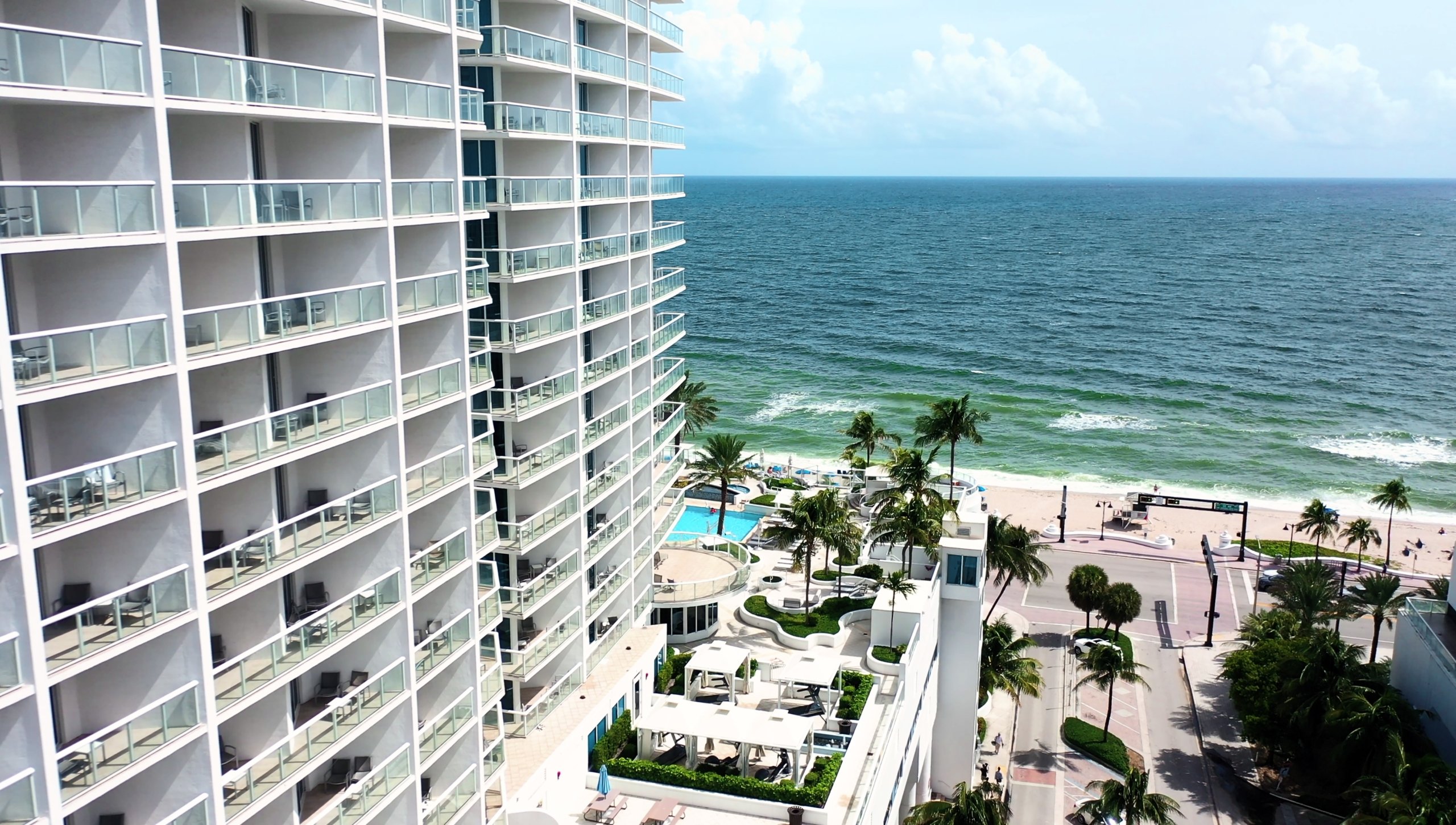 Exterior facade of the Fort Lauderdale Beach House resort showing the beach and emerald water of the beach.