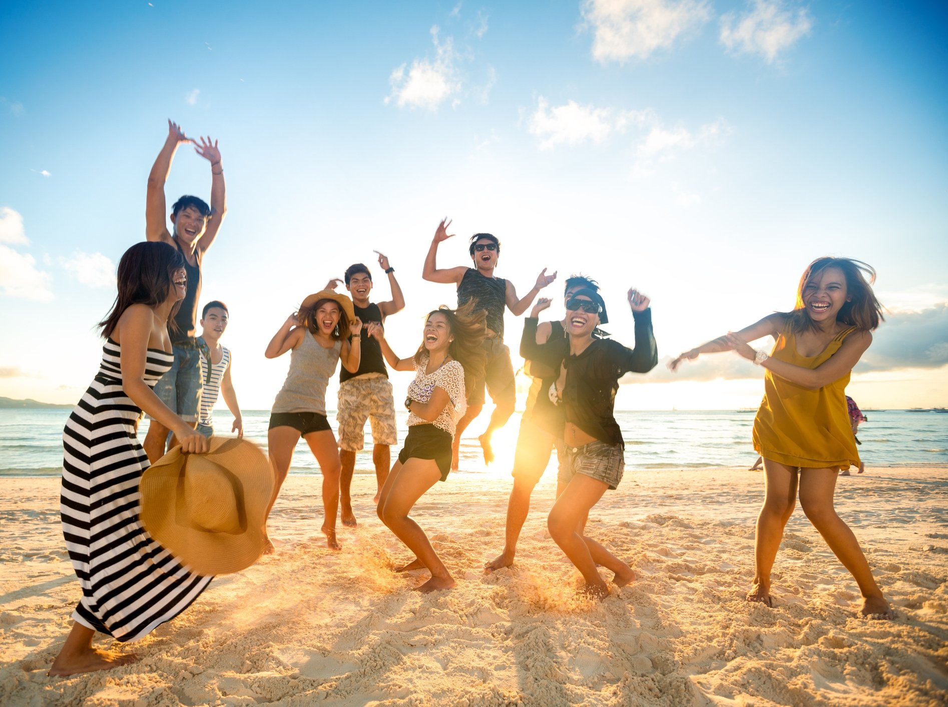 A group of people dancing and smiling on the beach at sunset