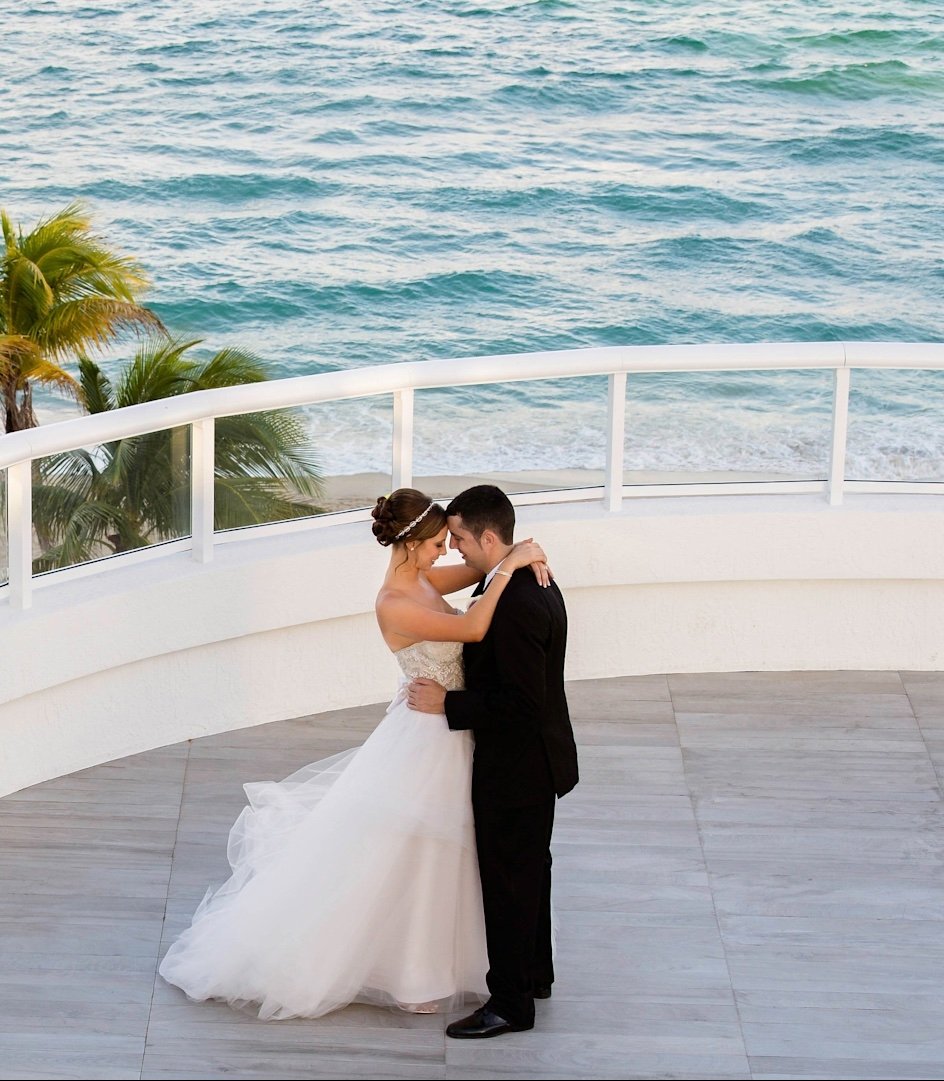 A newly married couple embrace on a patio overlooking palm trees and the ocean