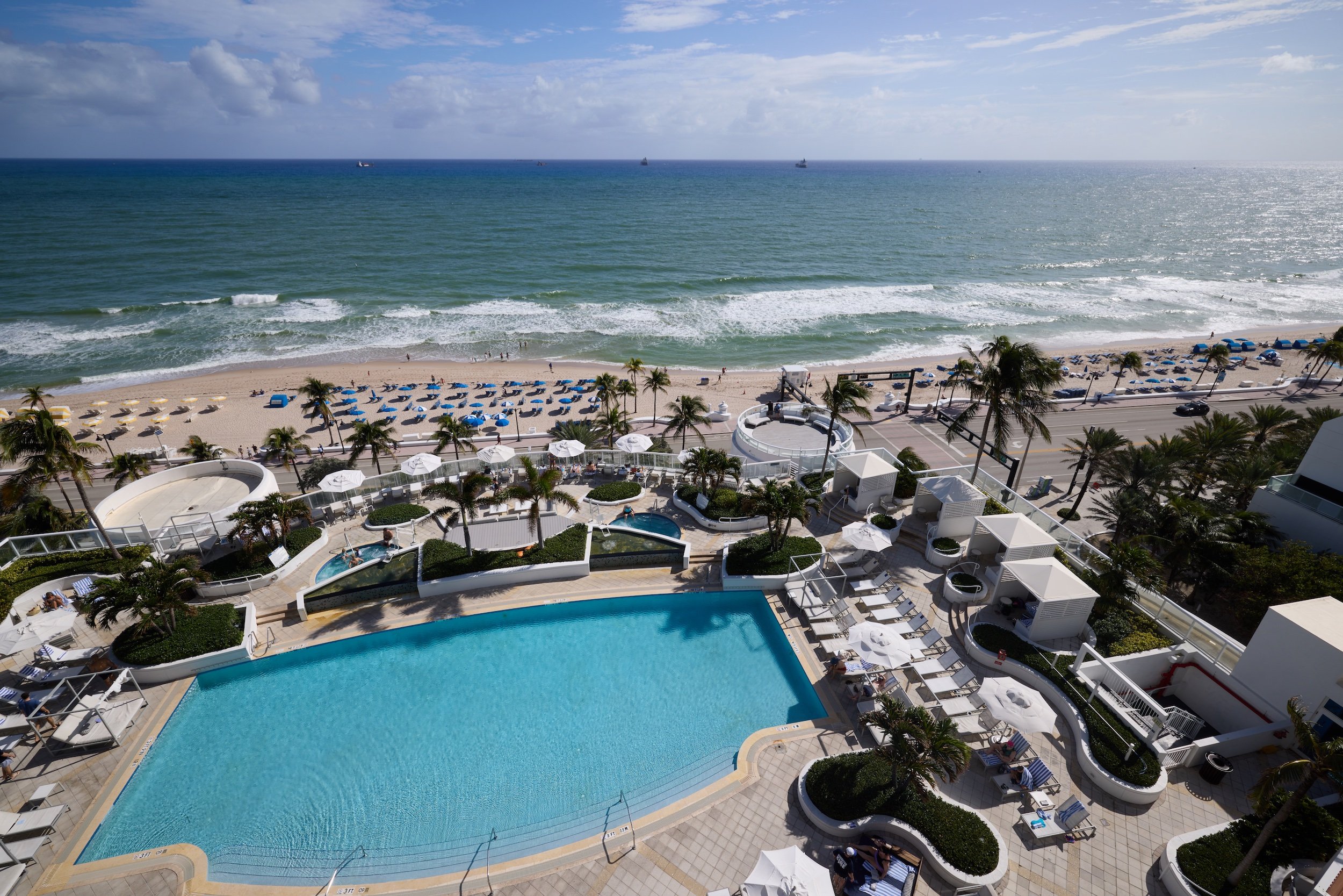 Aerial view of an outdoor pool surrounded by cabanas that looks out on the ocean