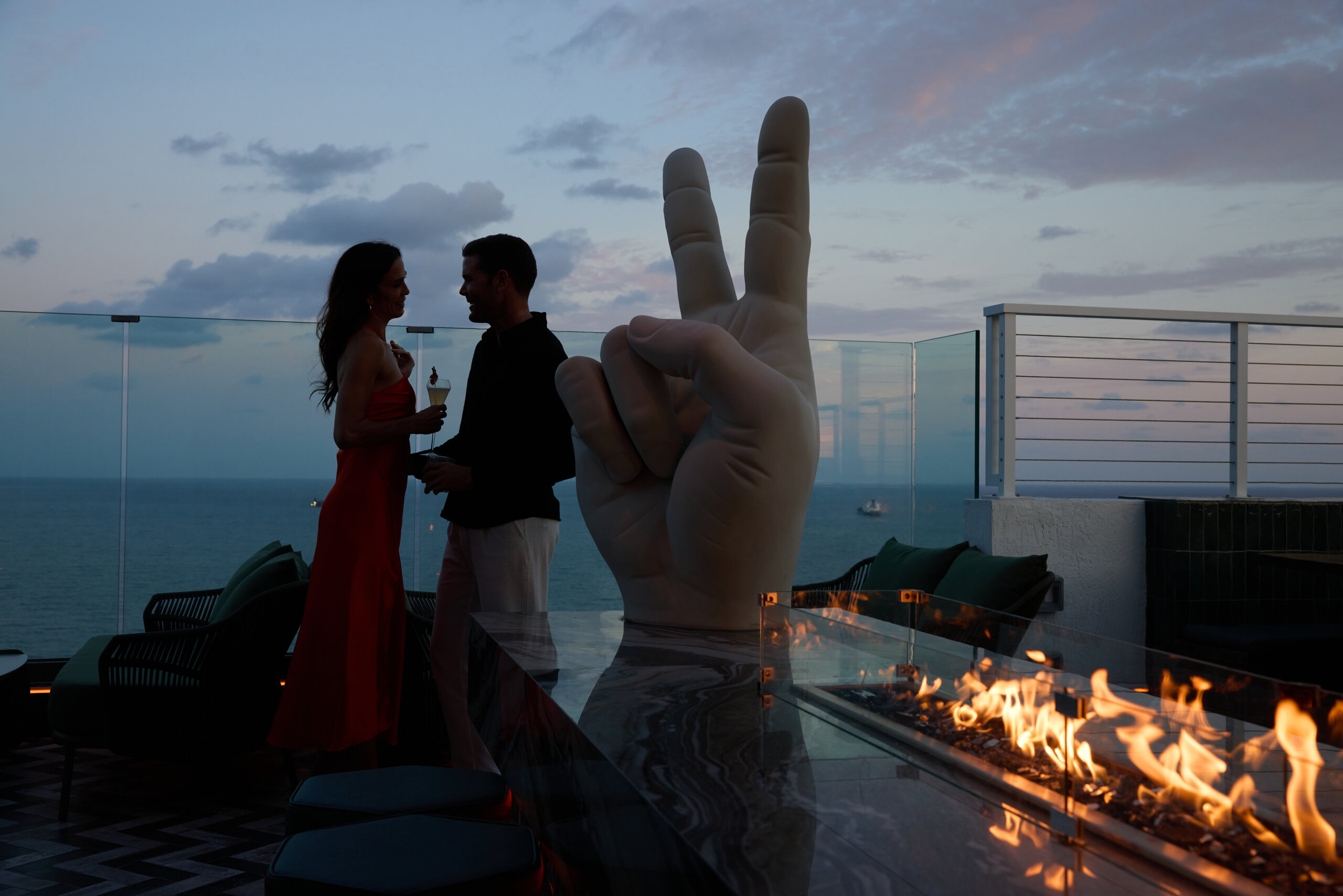 A couple stands next to the peace sign statue and fire table at Nube rooftop restaurant at evening