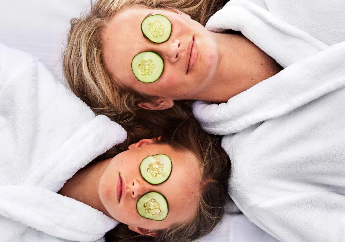A mother and child relaxing in white robes recline during a spa treatment with cucumber slices over their eyes