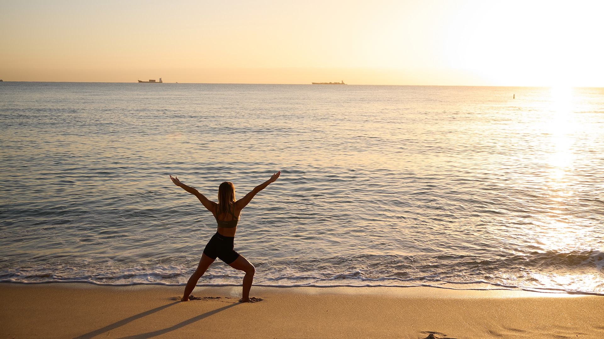 A woman does yoga on the beach at sunrise