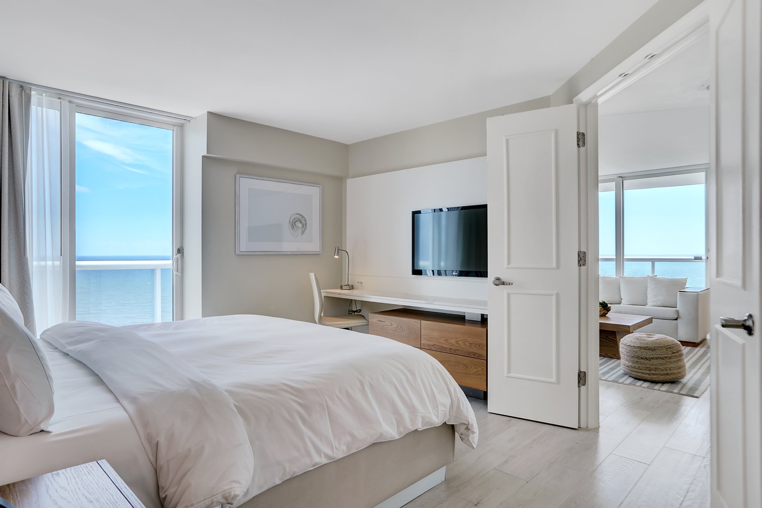 A bedroom with white sheets bed and small desk and chair