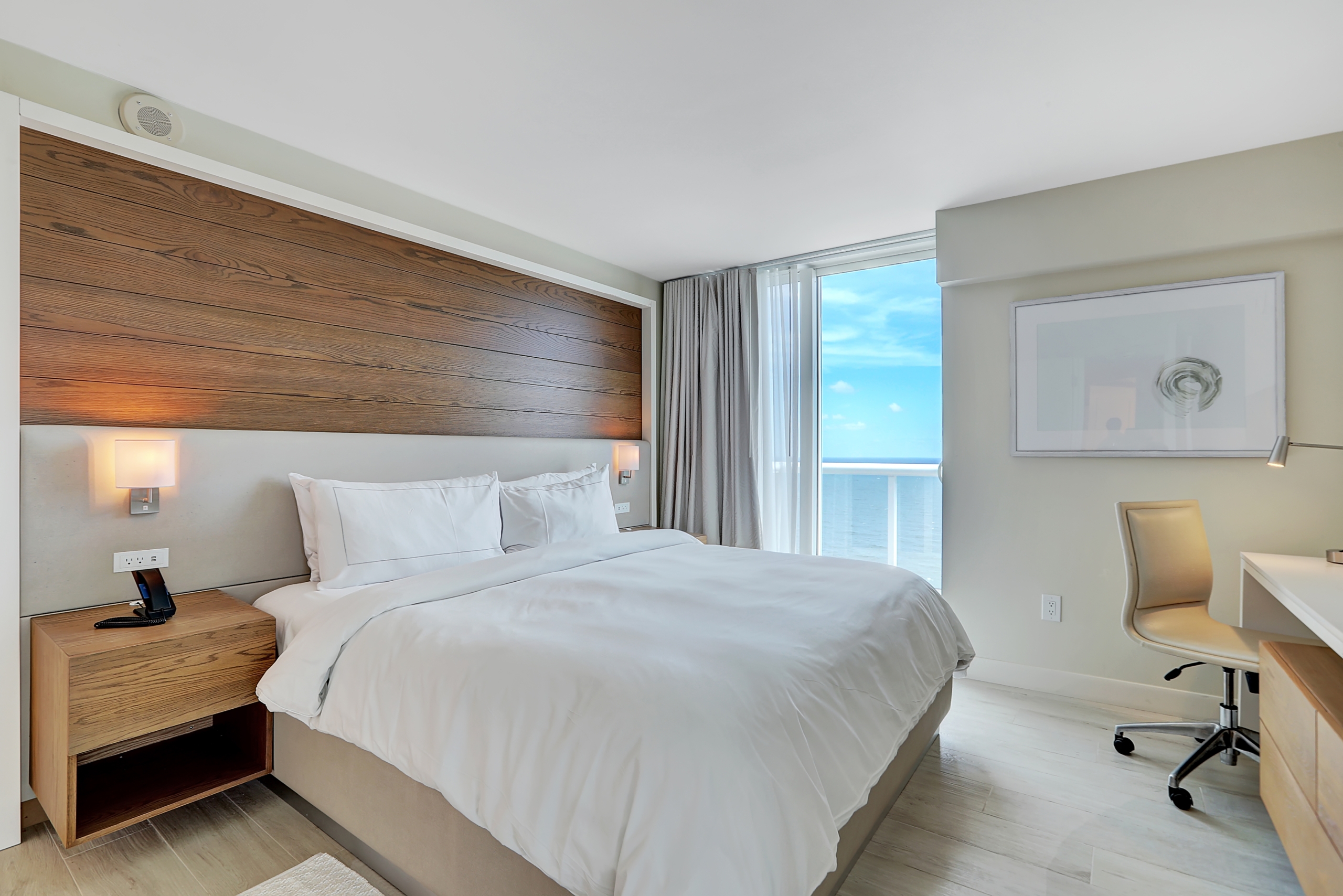 A king bed with white sheets next to large window of ocean view