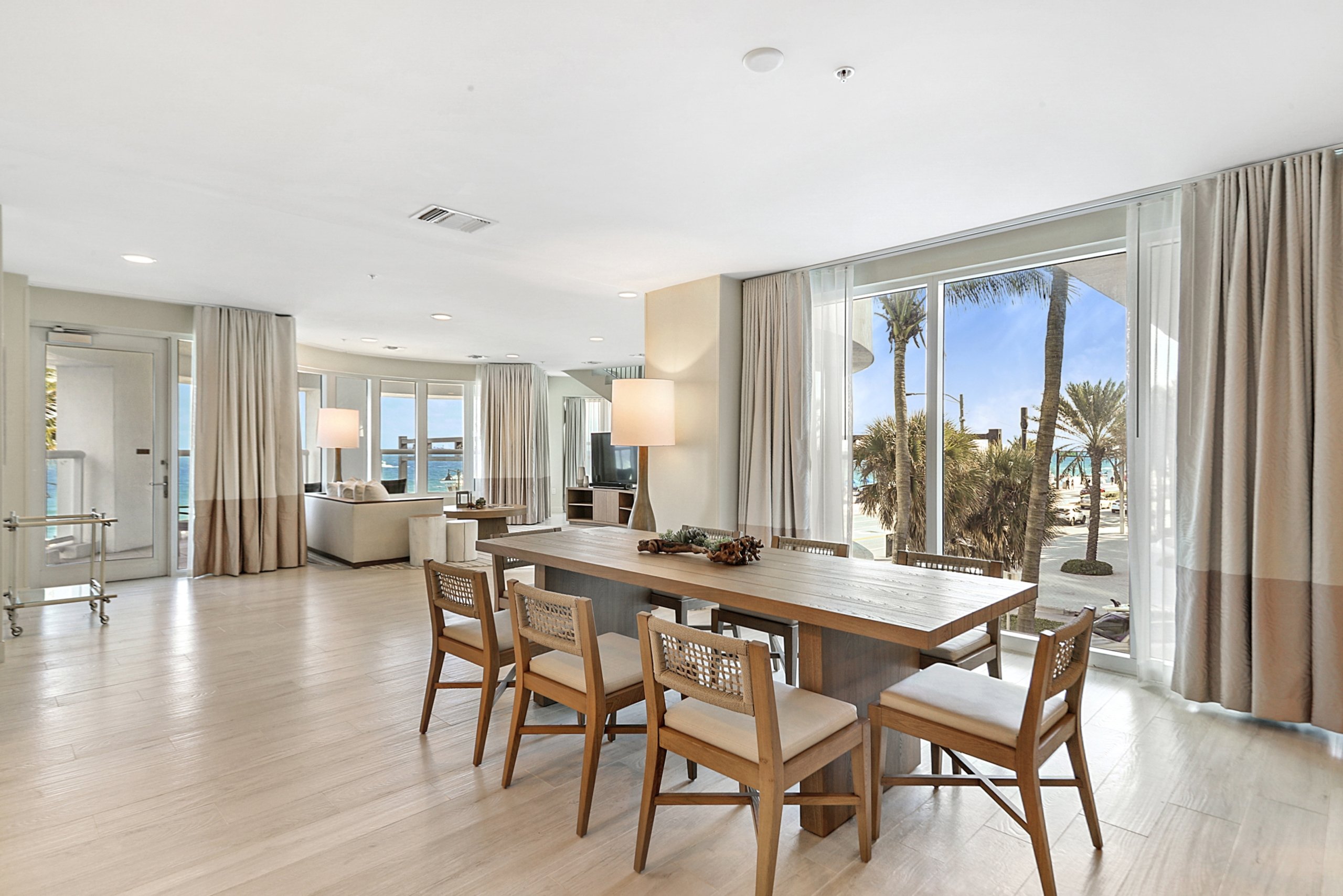 a long wooden dining table, comfortable chairs, white couch in large living room with several windows to the beach