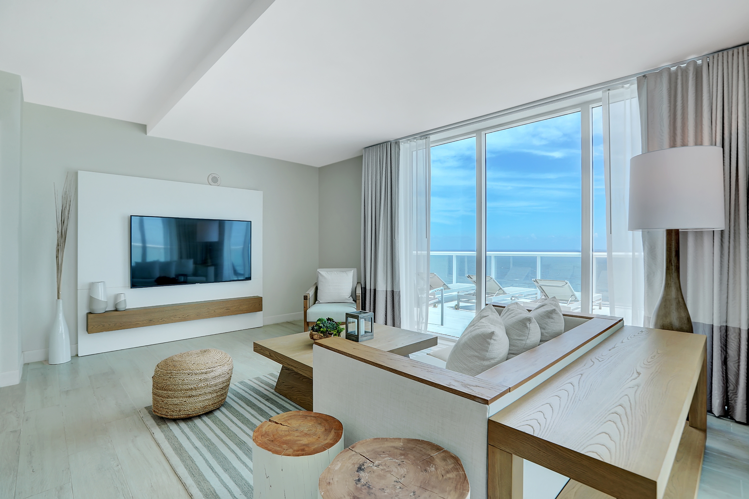 wooden and white furniture in living room with large window to large balcony of ocean view