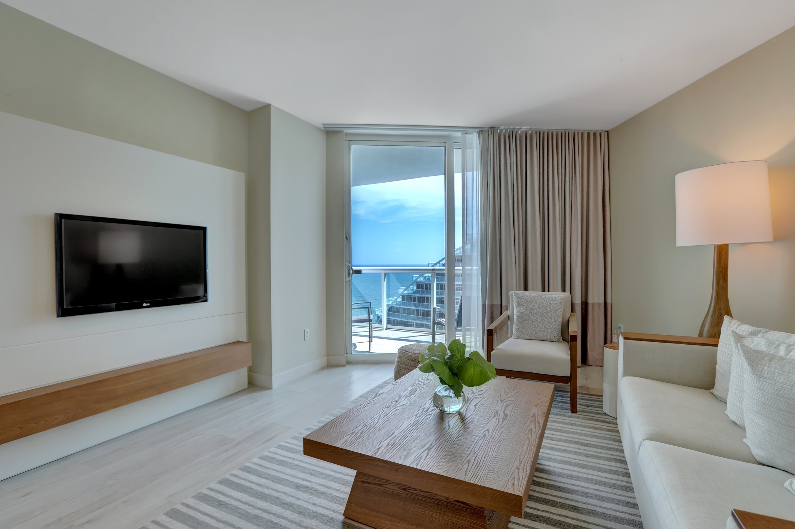 White modern couch, arm chair, wooden tea table, and a large window to balcony in modern living room