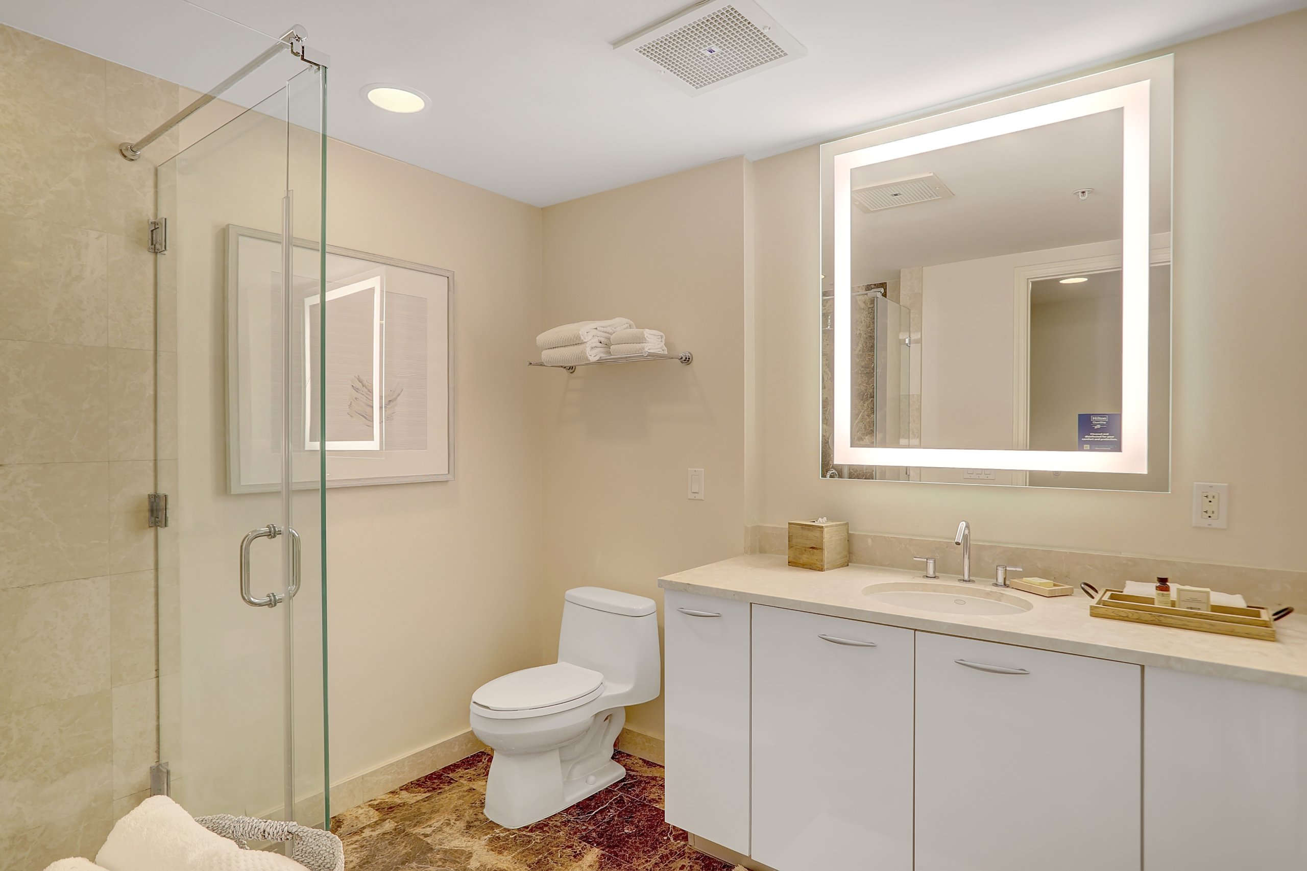 Shower booth and sink counters with hotel amenities and bright mirror in marble bathroom