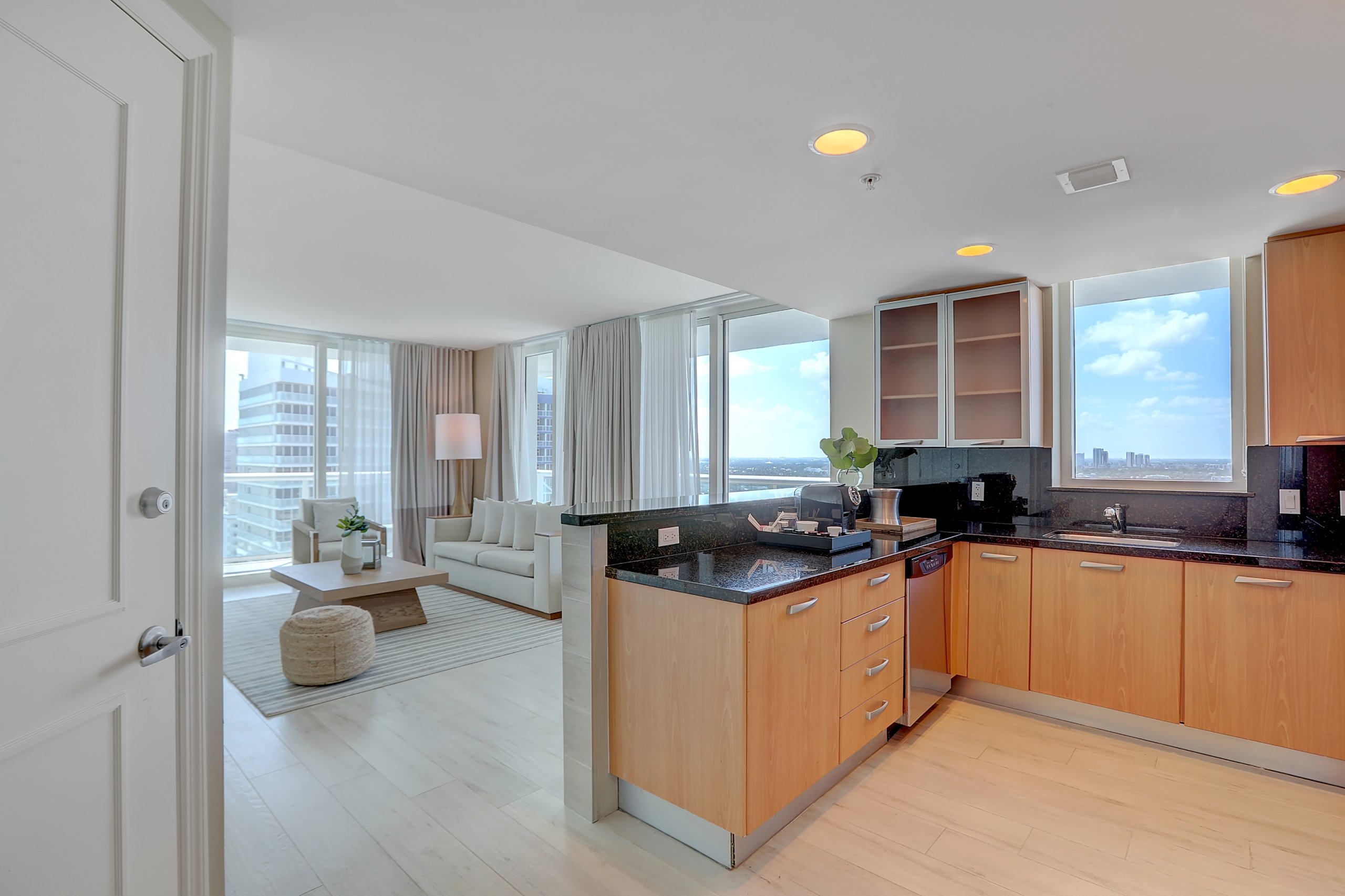 Kitchen space with black counters and wooden shelves and living room with white couch and tea table with large window to balcony