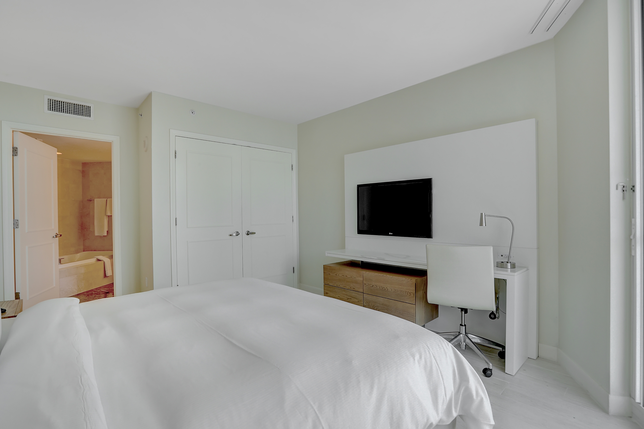 A bed with white sheets, modern chair and desk in bedroom