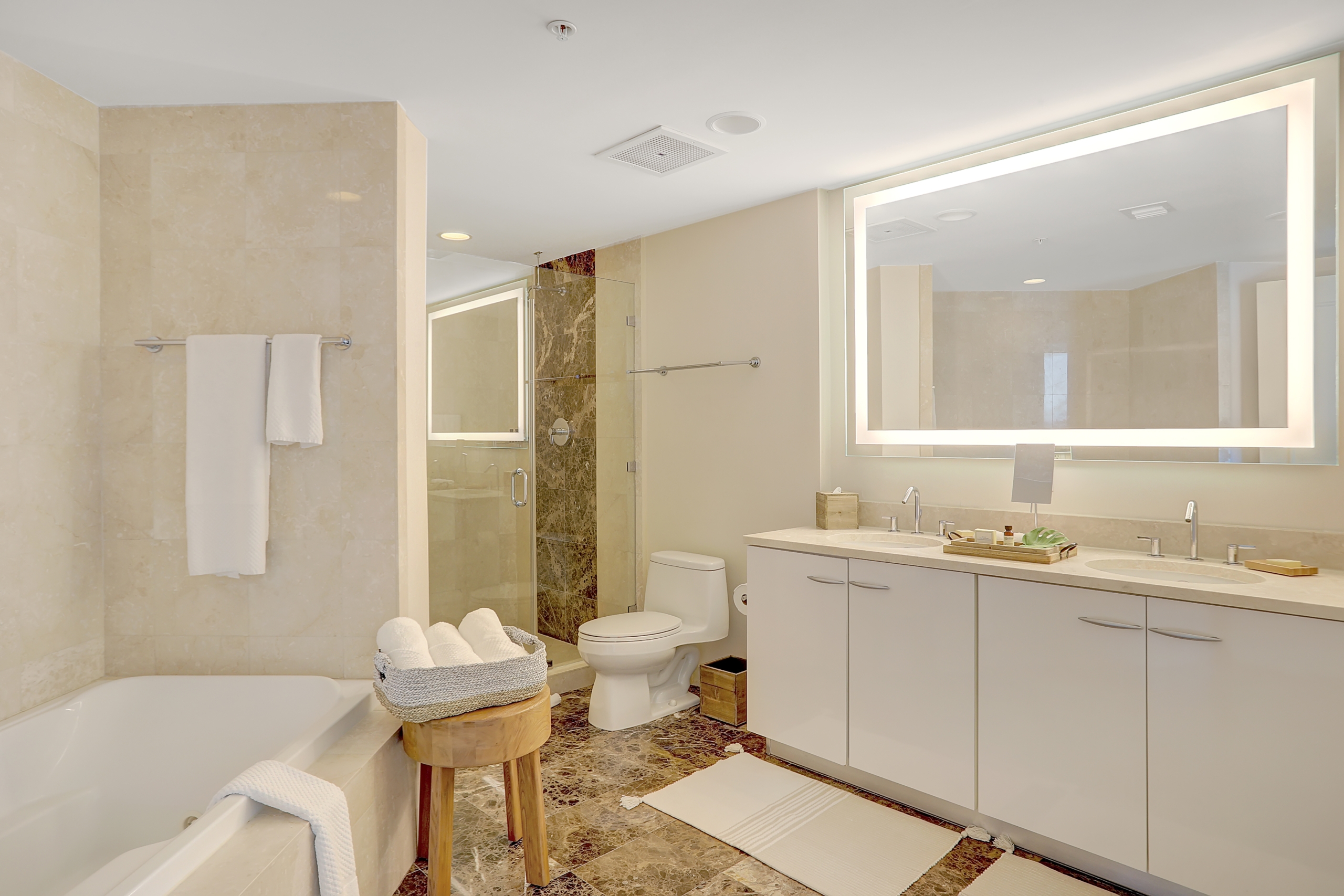 white bathtub, shower booth, wide counter with two sinks and big bright mirror in bathroom