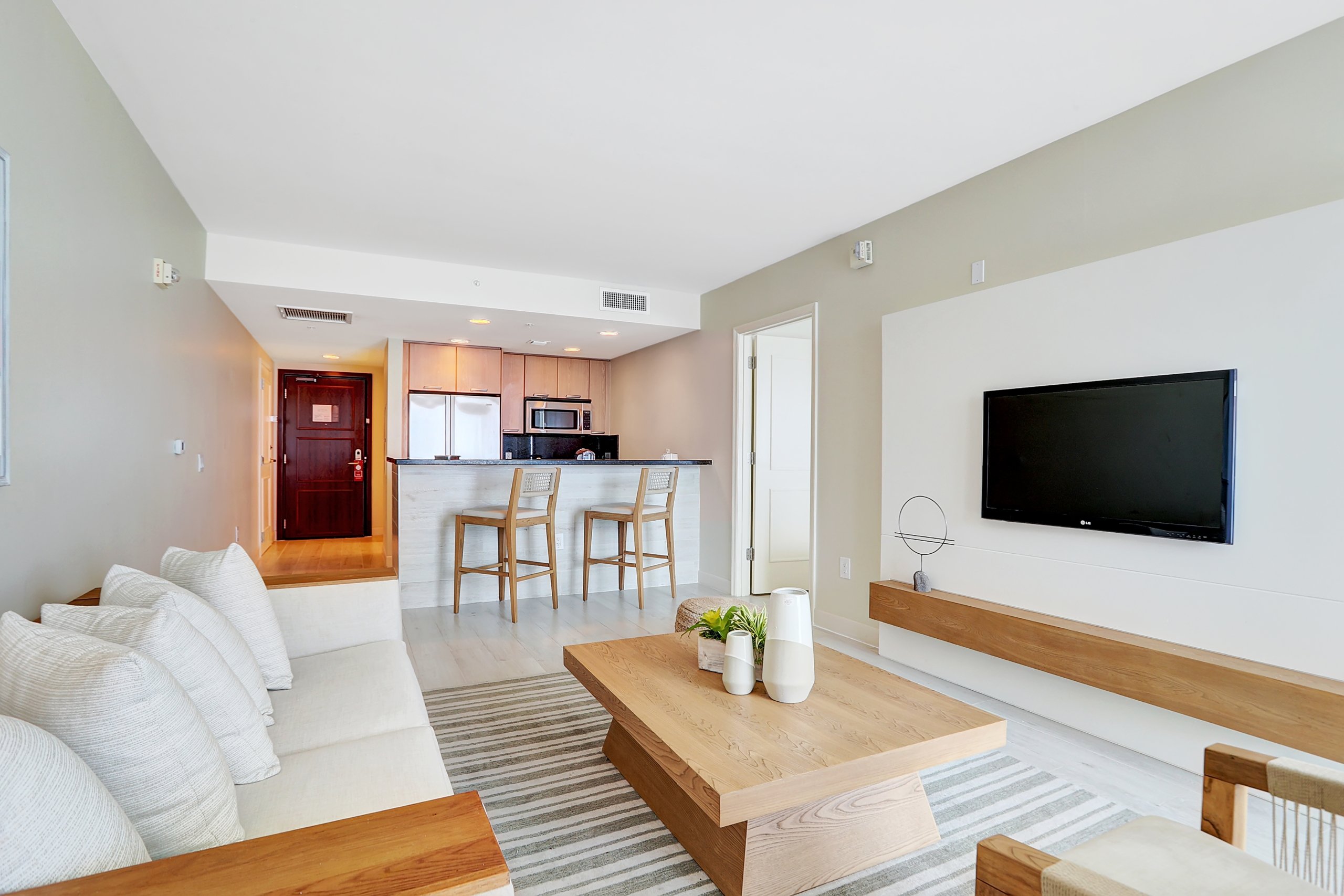 A living room for white comfortable couch, wooden tea table, and modern kitchen area with tall chairs