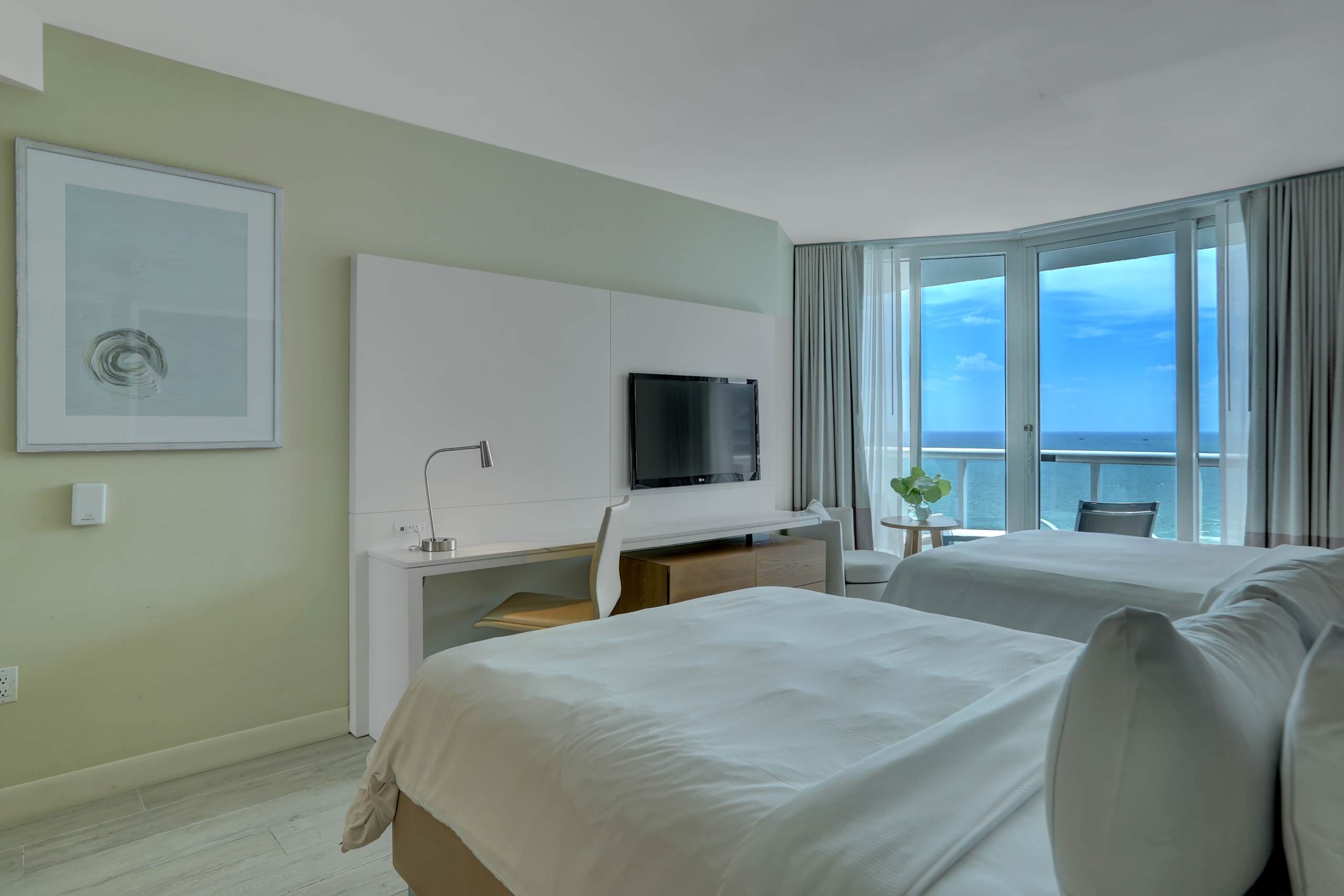 Two queen beds with large window to balcony and a painting on green coloured wall in modern bedroom