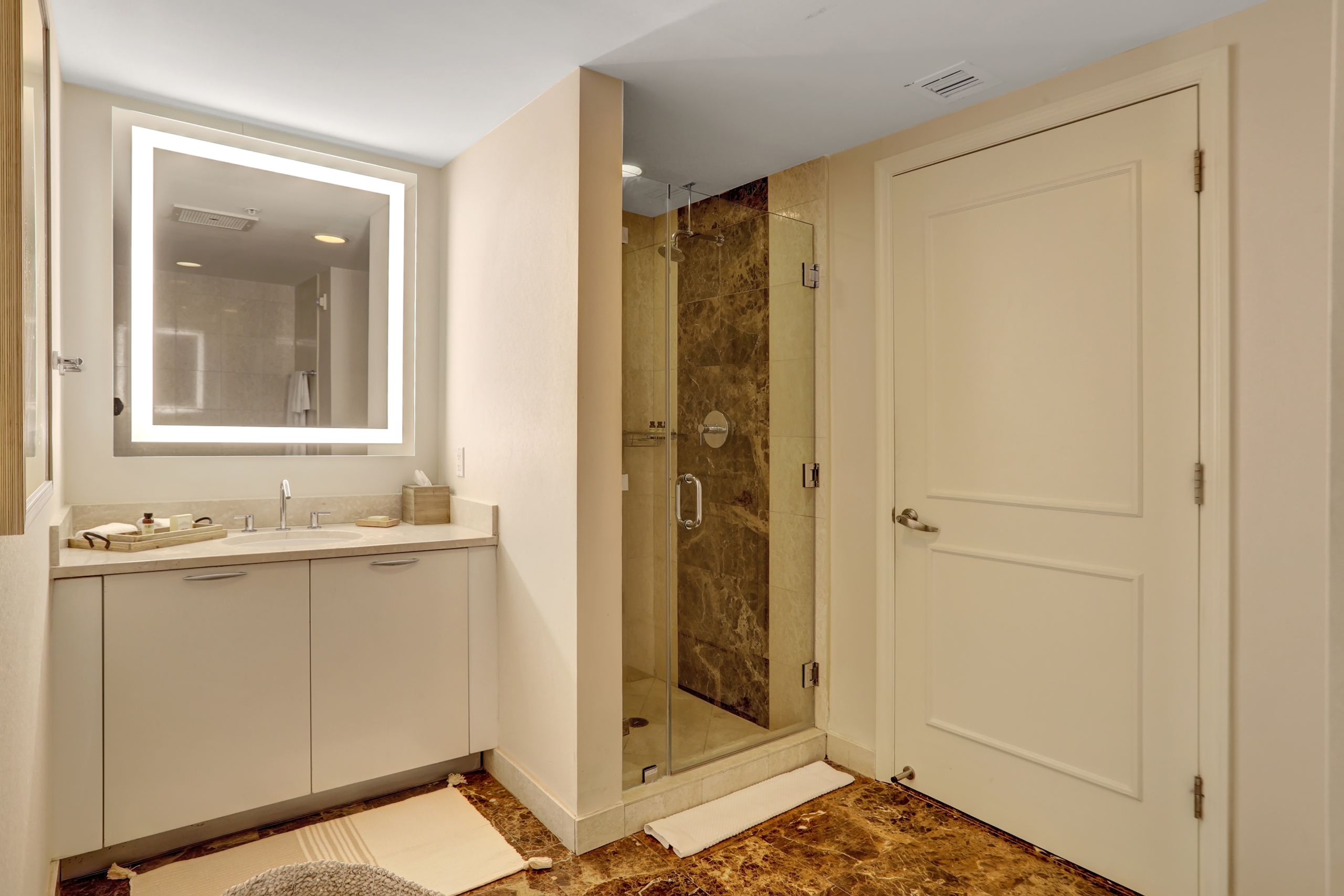 A sink counter with hotel amenities and a bright mirror and shower booth in bathroom