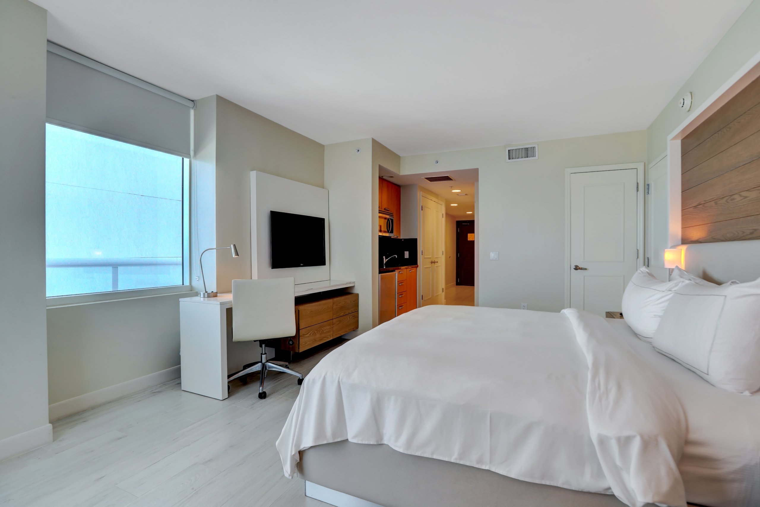 King bed with white sheets, white desk and chair, modern kitchenettes in modern studio suite