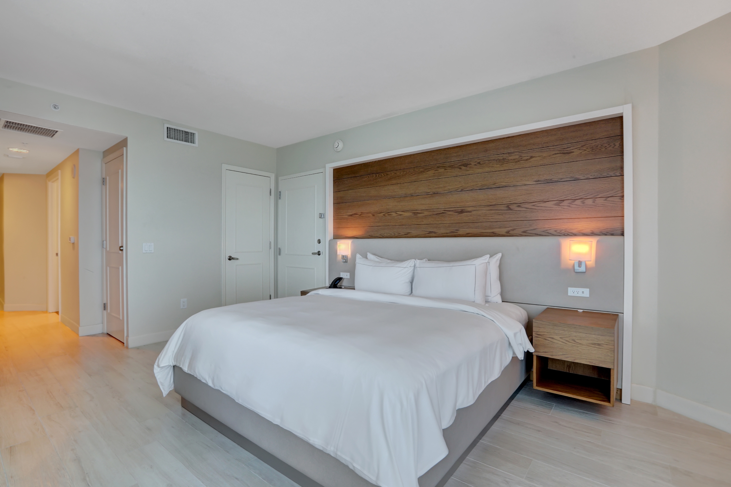 King bed with white sheets on wooden wall in white toned bedroom