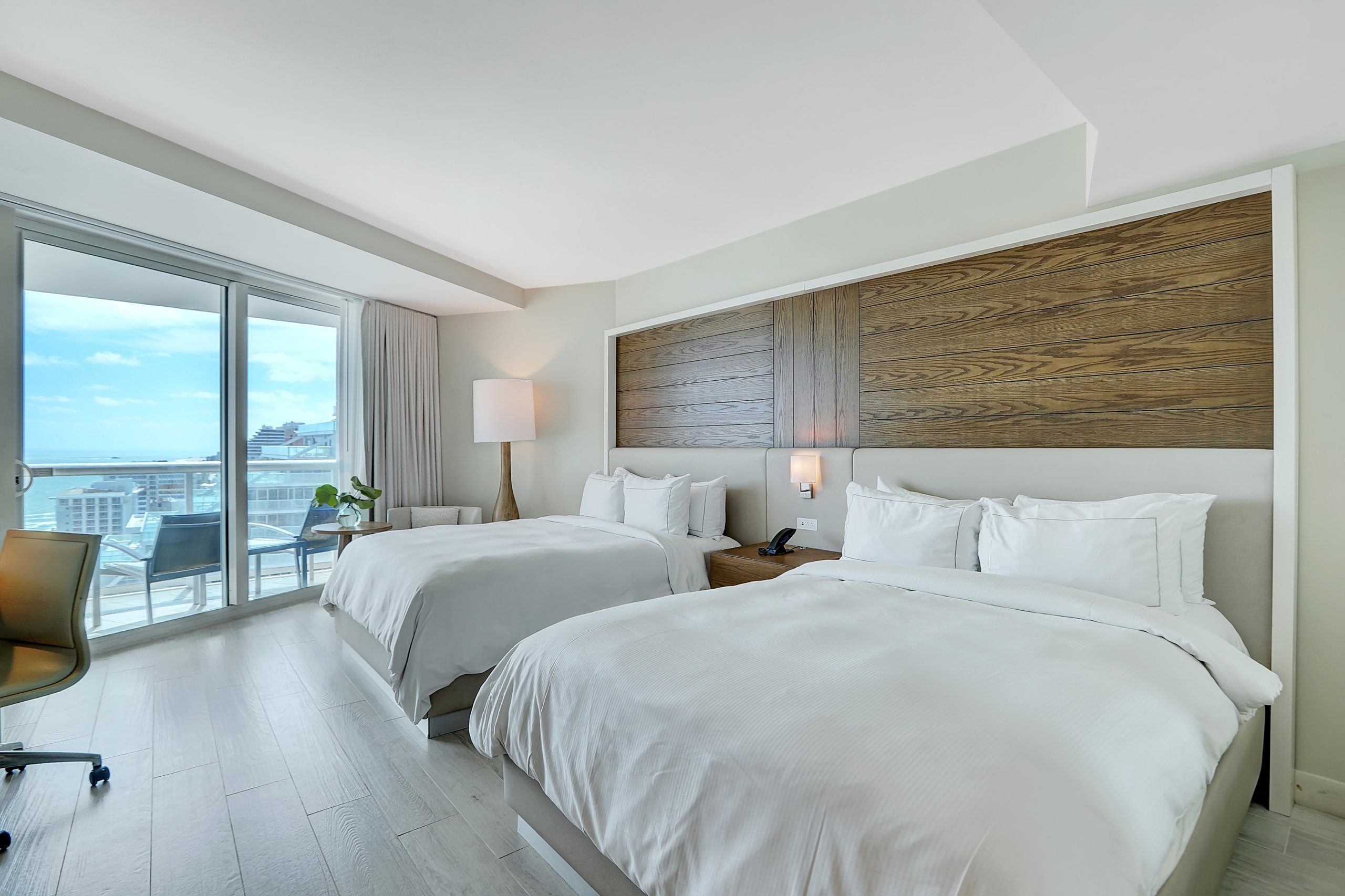 Two queen beds on wooden wall with large window to balcony in light green toned bedroom