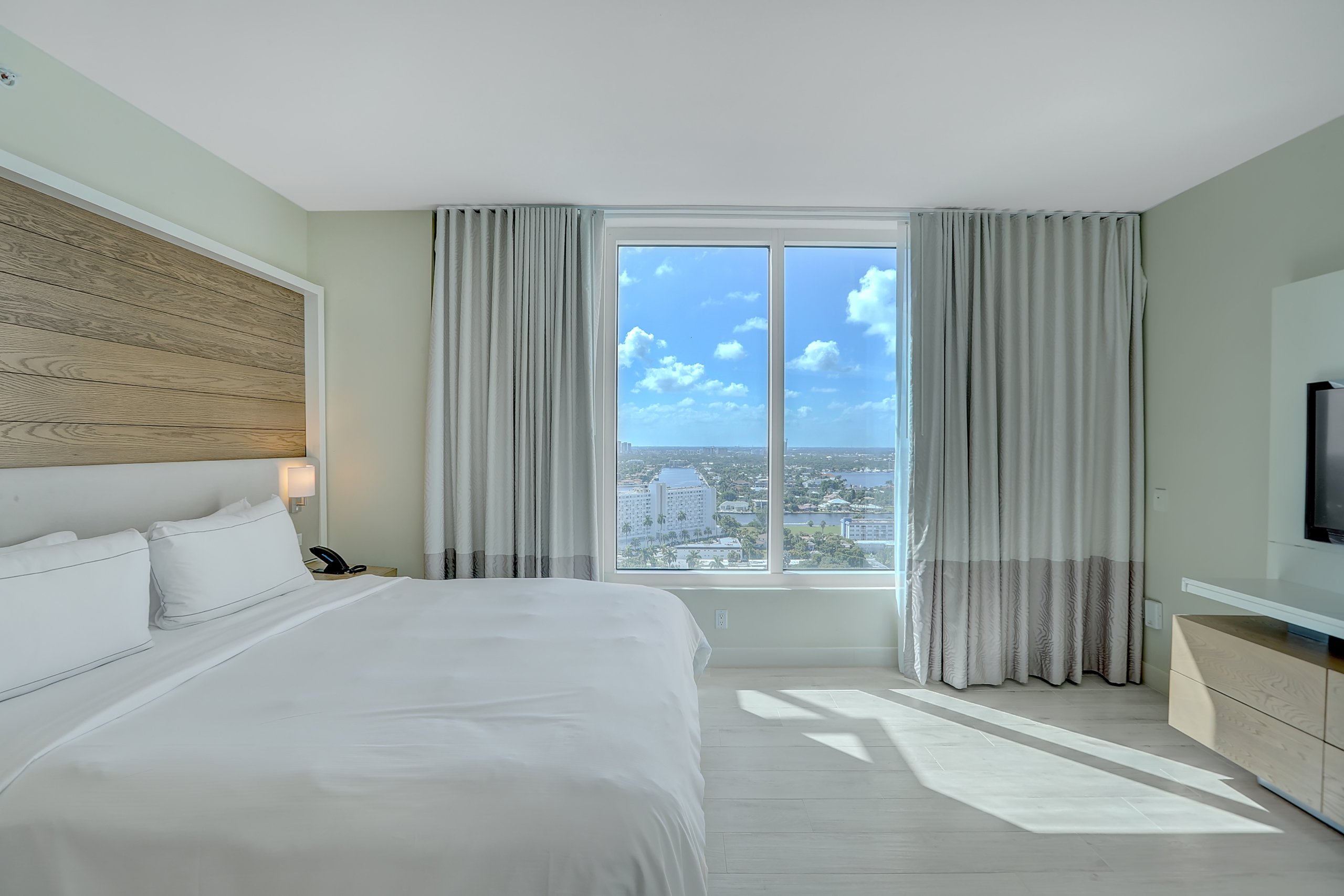 King bed with white sheets with large window in sunny weather