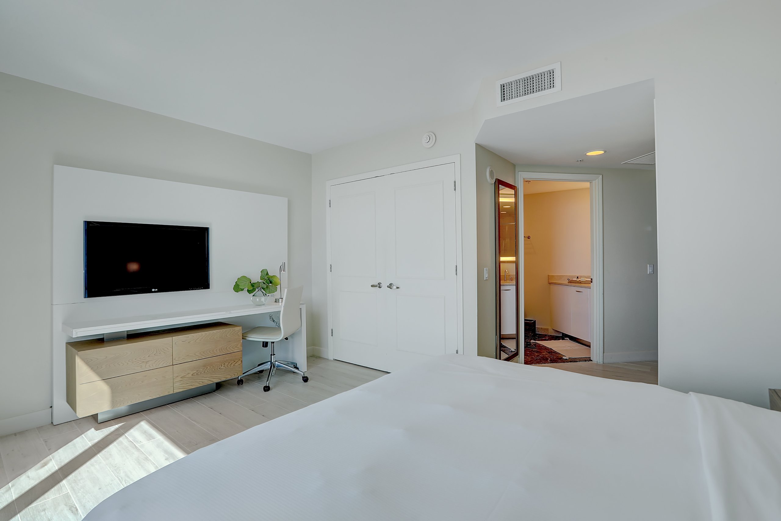 White desk and chair set, a tall mirror, white sheets bed in modern studio