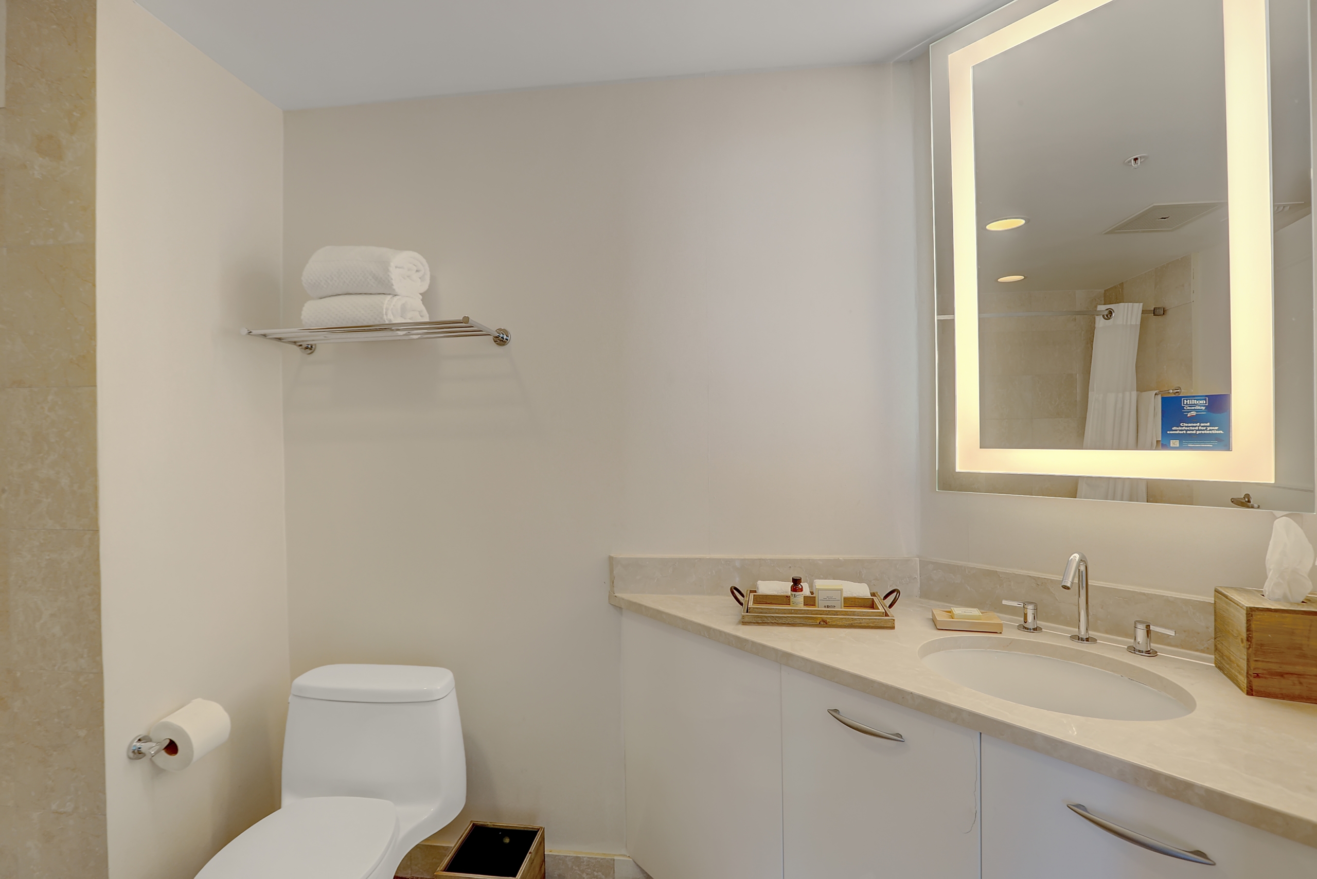 marble sink counter with hotel amenities and lighting mirror in white colored bathroom