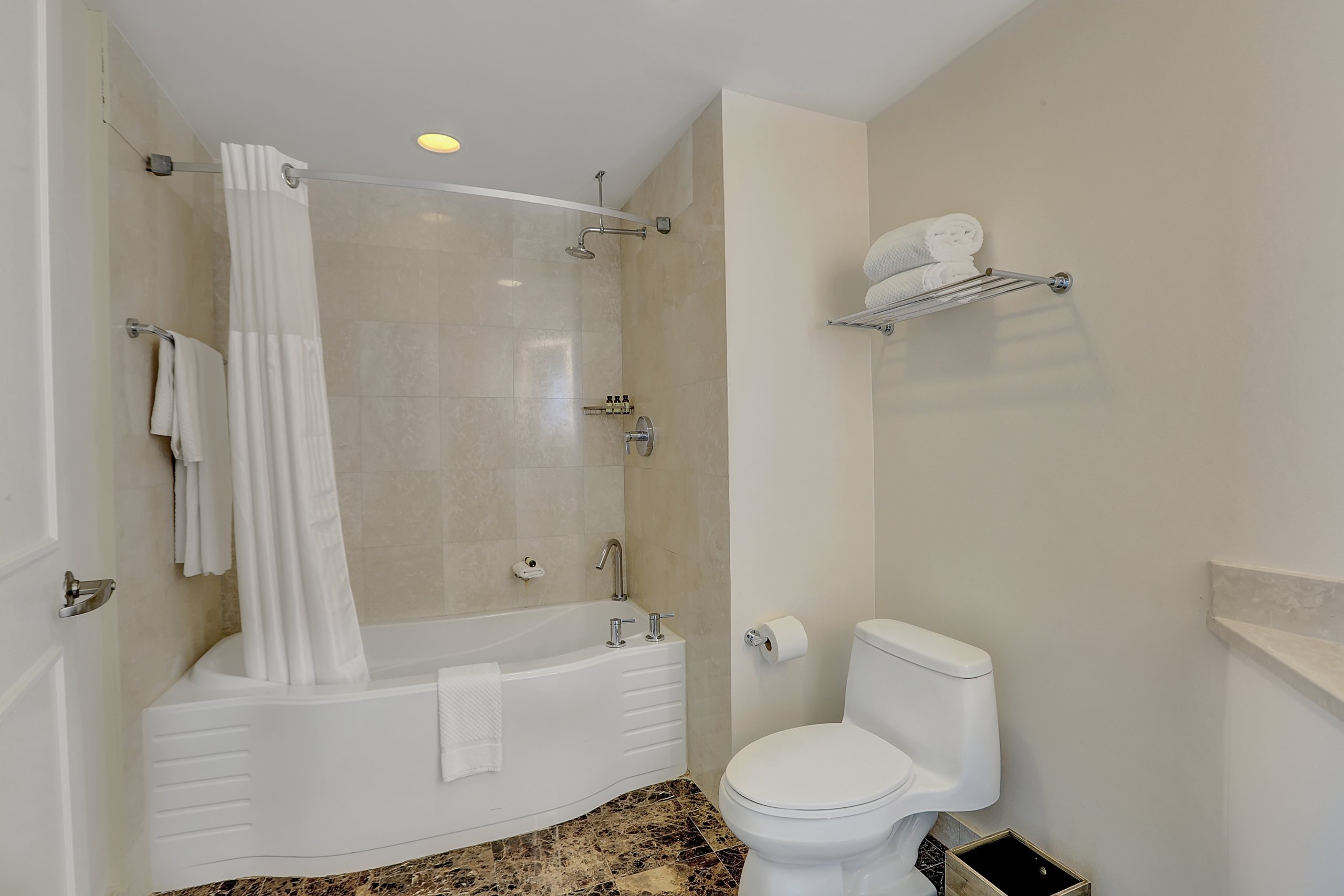 white bathtub and shower curtain with toilet in sand coloured marble bathroom