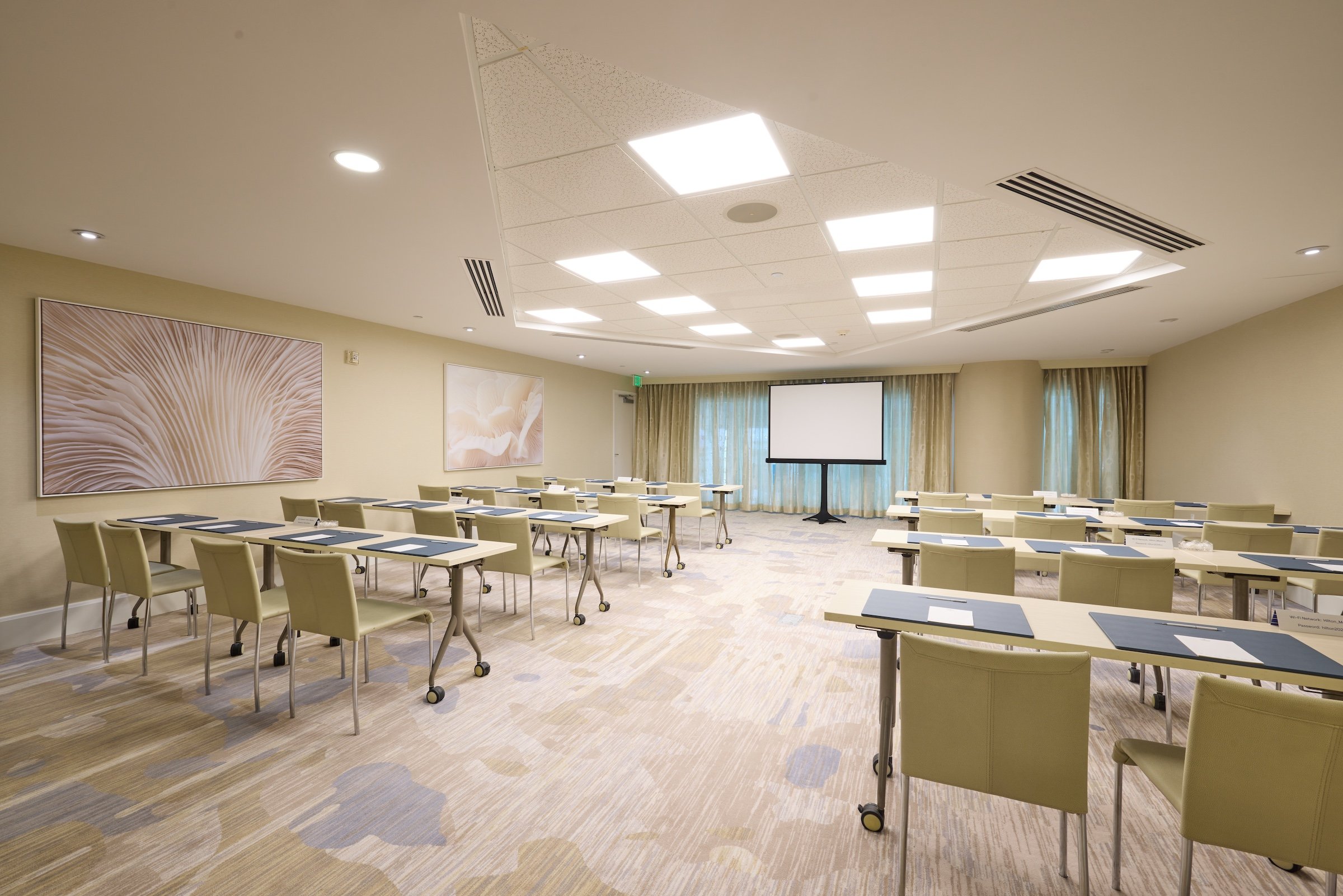 A bright meeting room with a large projection screen at the front of two rows of desks