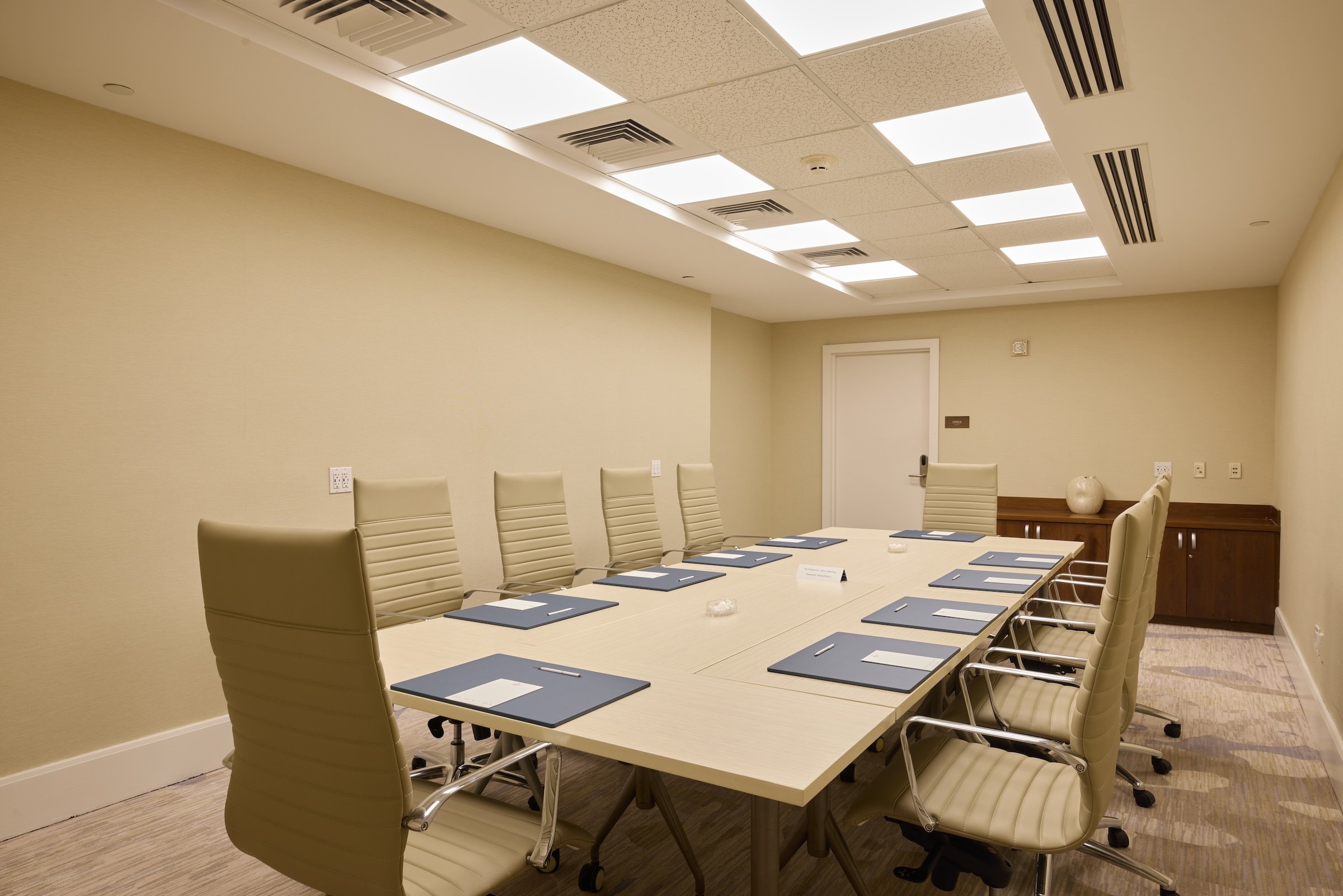 A boardroom style meeting room with a long table surrounded by padded chairs