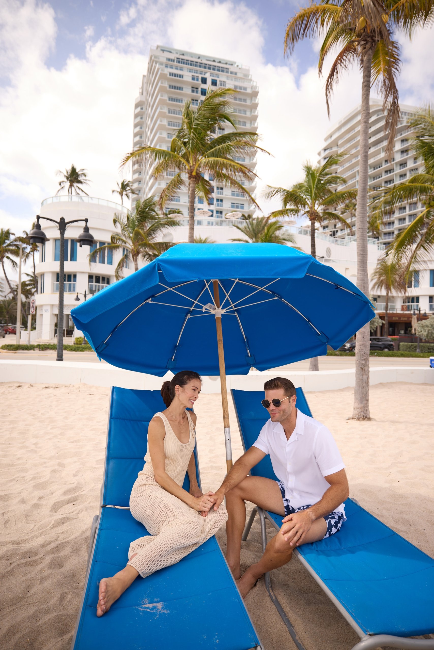 A couple sitting on the blue beach chair under parasol in front of the hotel