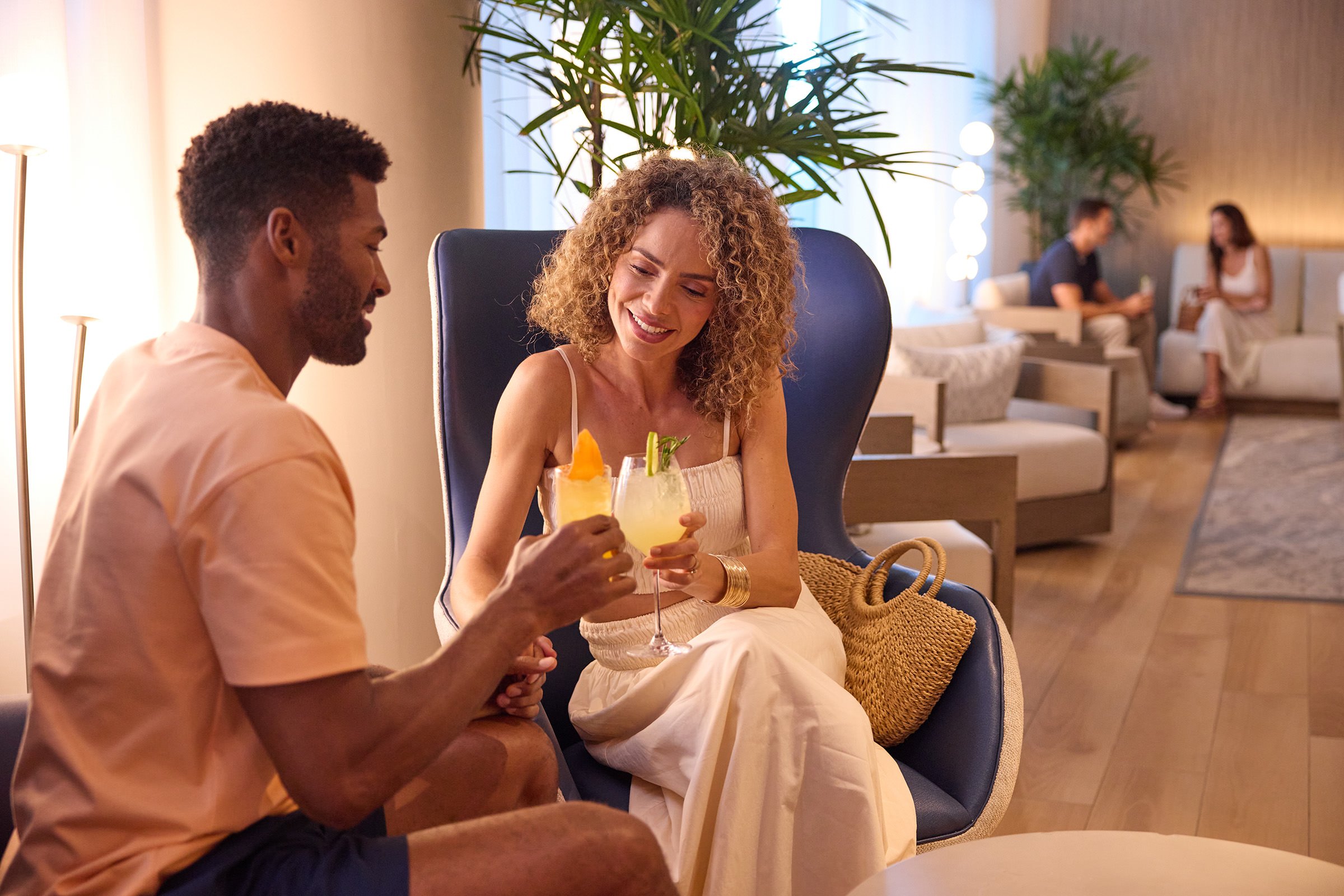 Couple sit on comfortable chair, cheering their cocktails in lobby