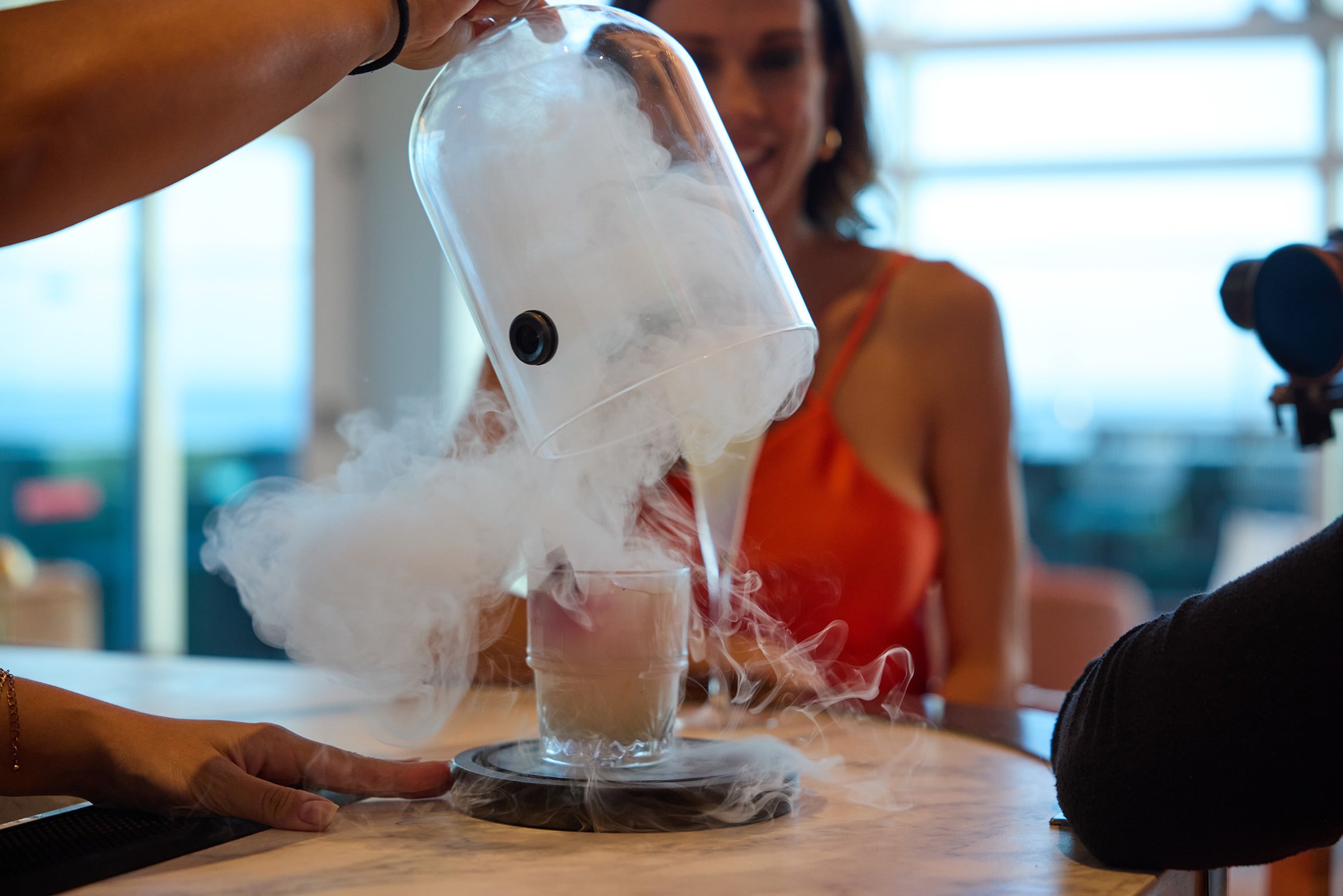 A woman watching smoked cocktails from bartender making at Barto