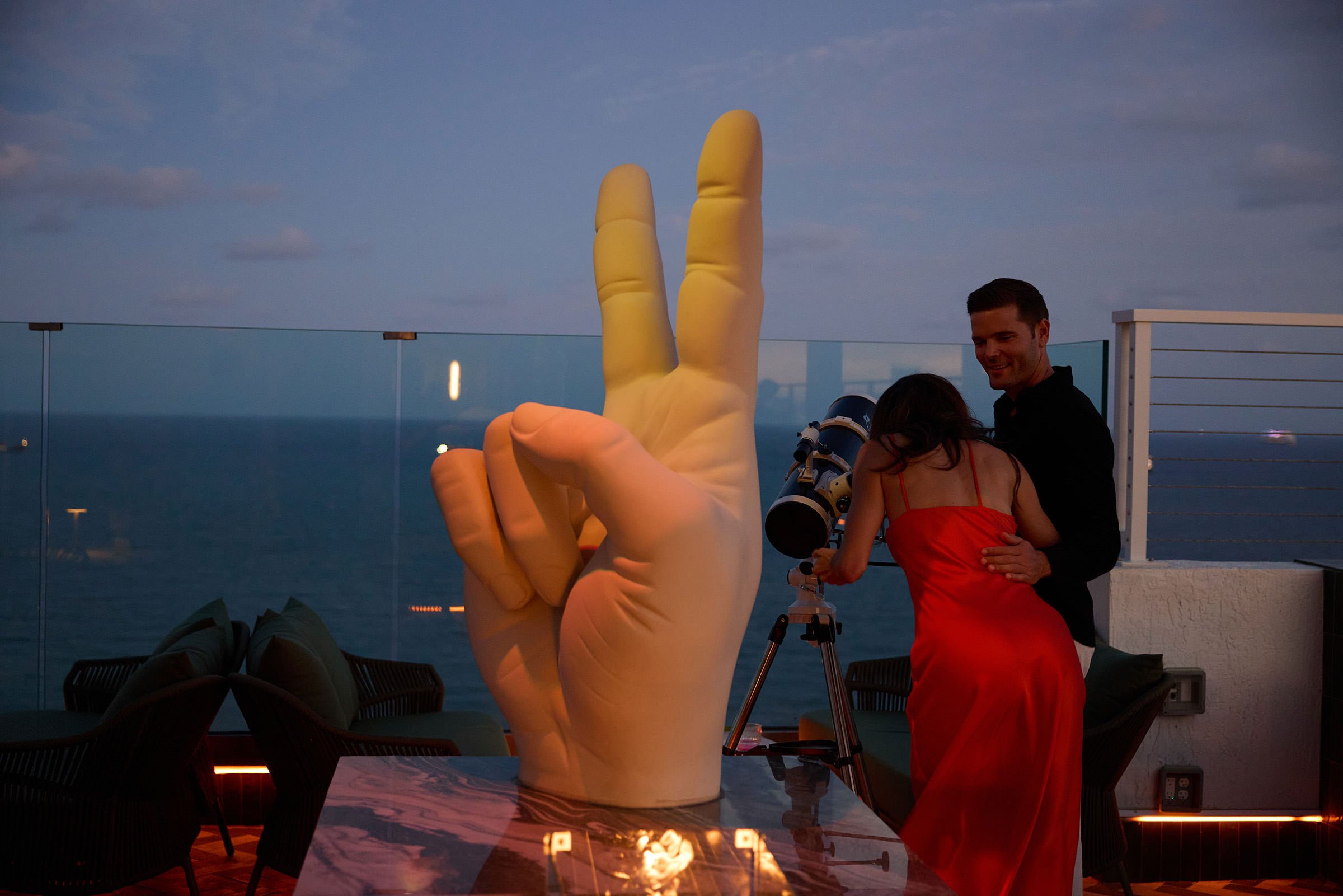 A couple looking at telescope behind V shaped statue at night