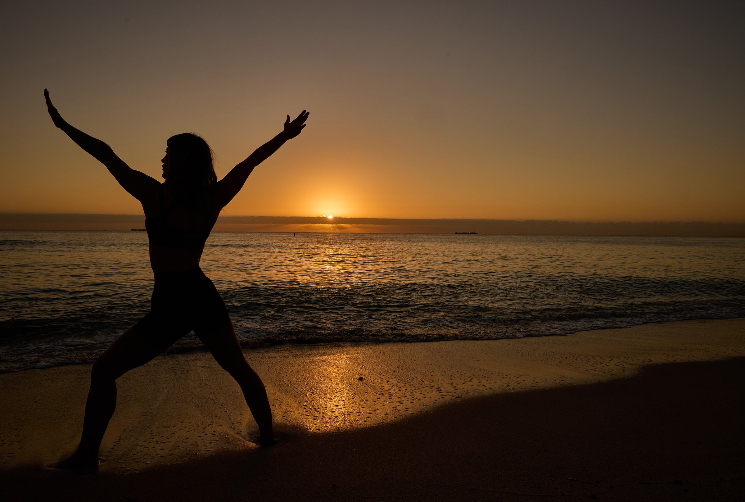 Women working out yoga on beach during sunrise