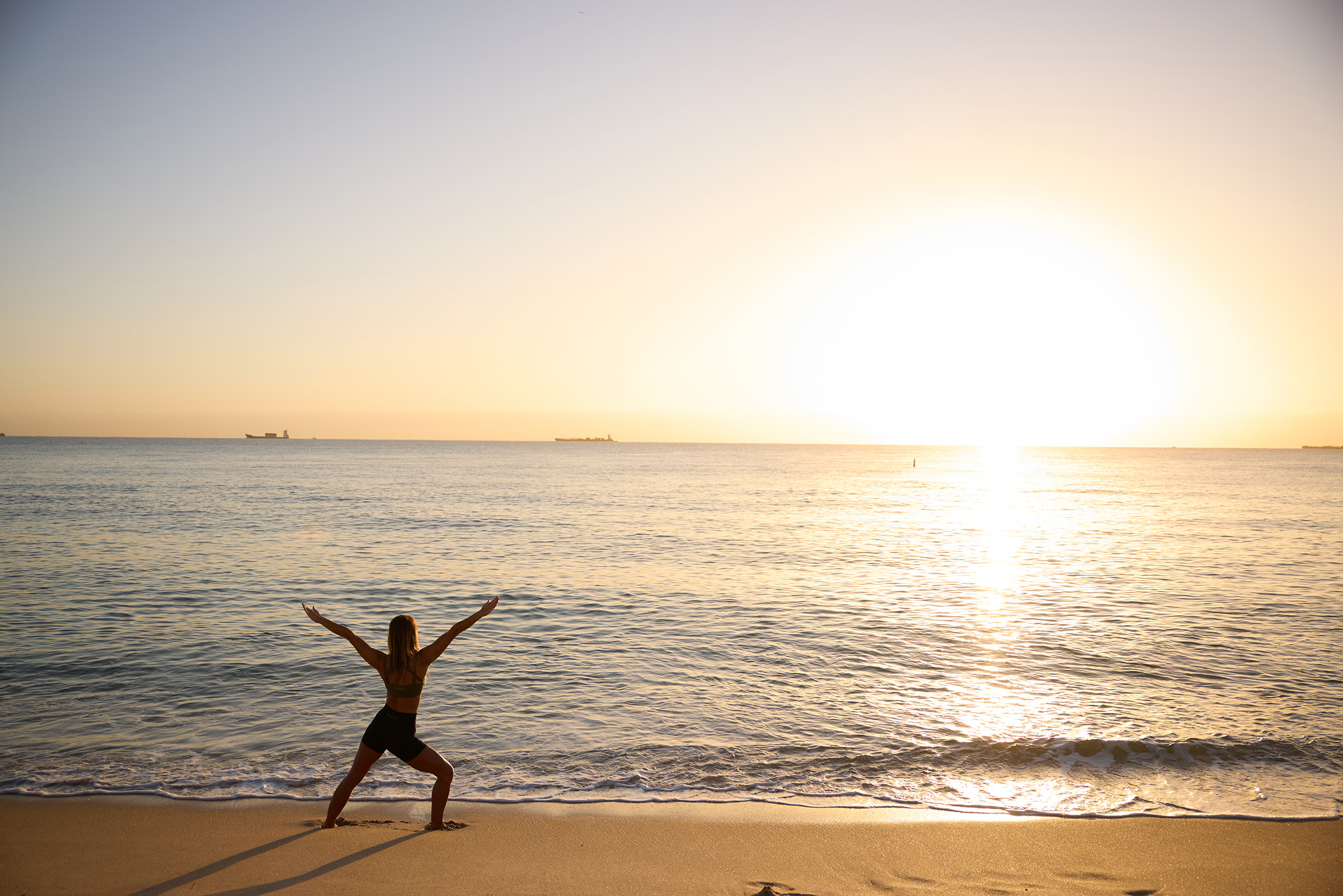 Woman stands on the Fort Lauderdale beach at sunrise while she performs the yoga warrior pose 2.