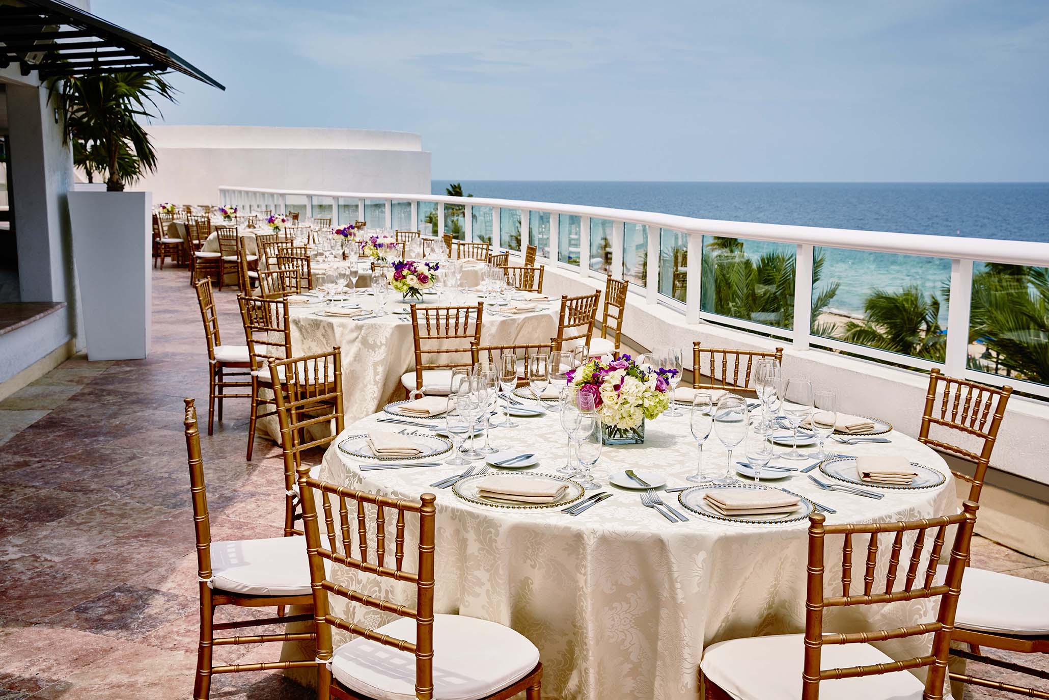 Exterior table settings at BalQony. Bronze chairs with white cushions around embroidered cream colored tables