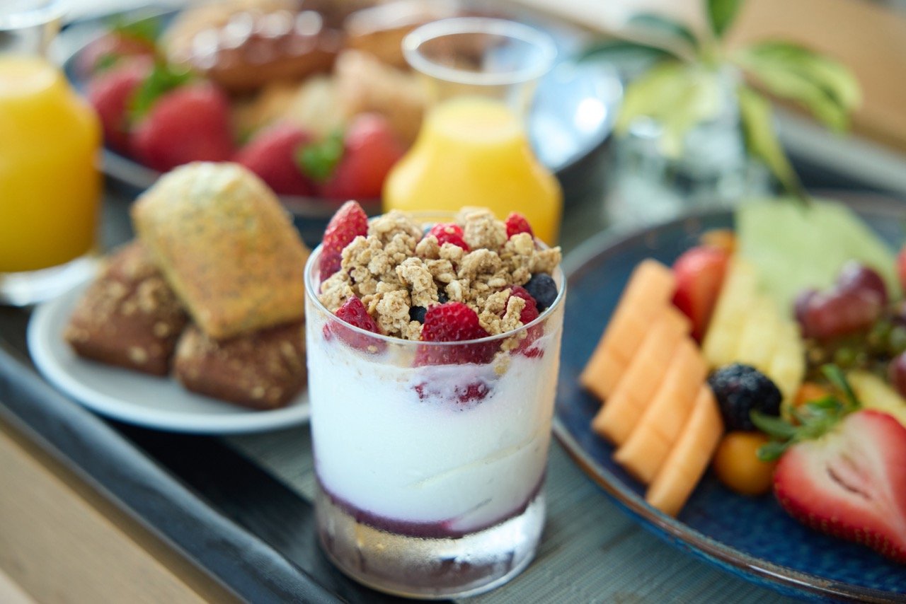 a fruit and granola yogurt parfait against a unfocused background of various breakfast foods