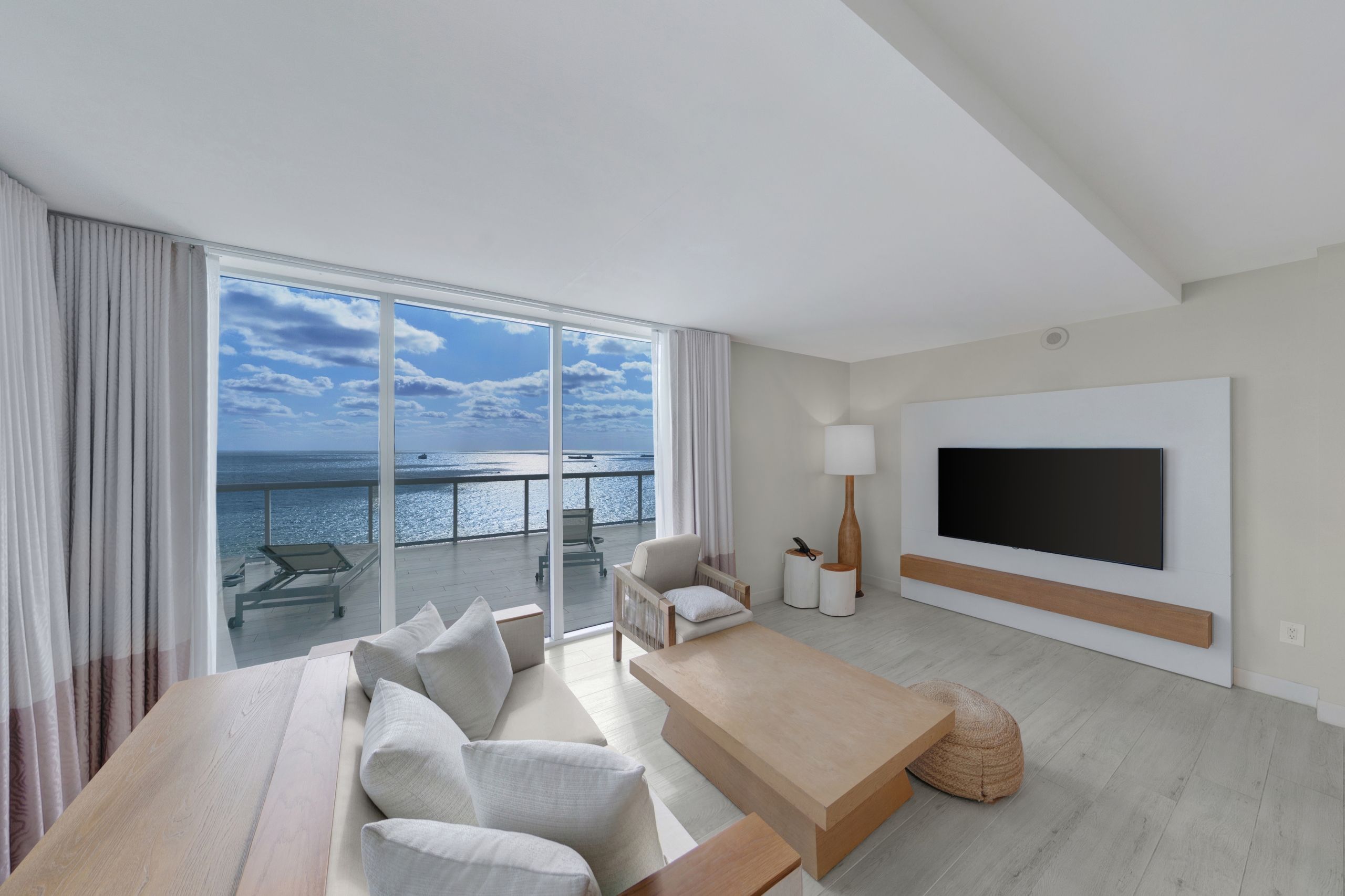a clean white room with wood furnishings and a ocean view balcony in the background.