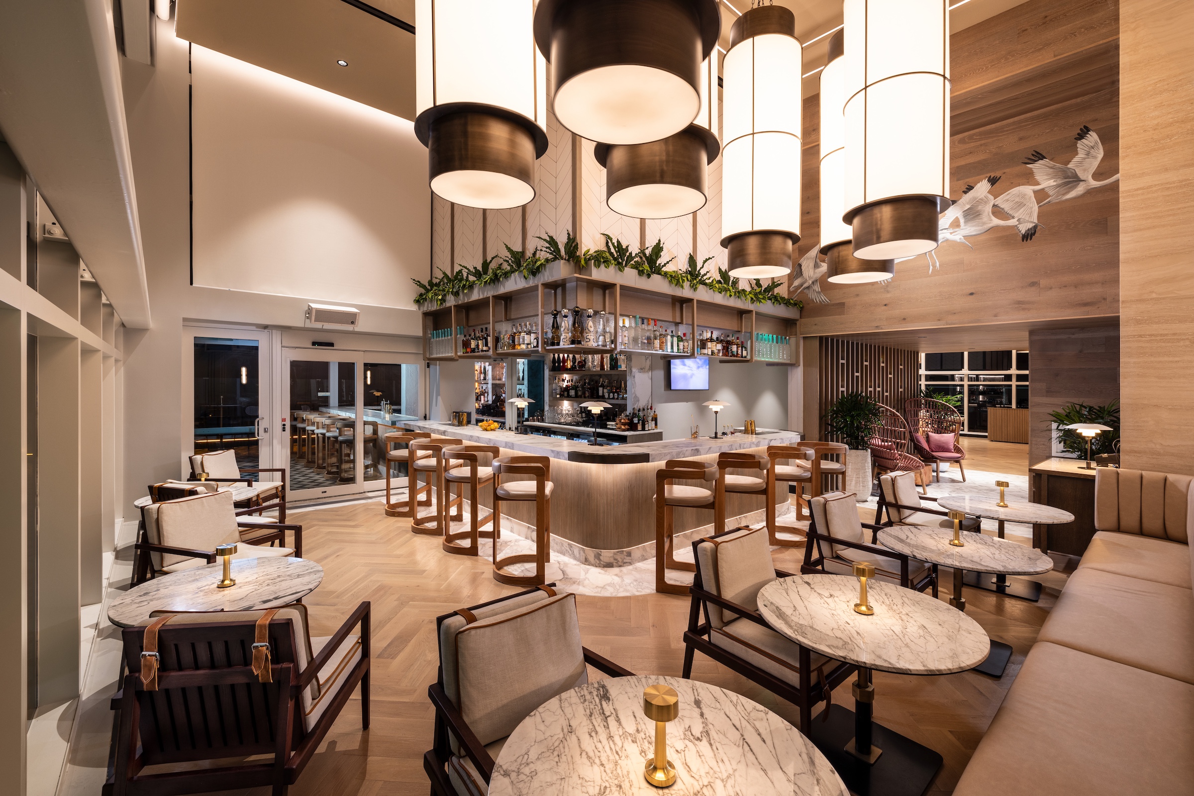 A corner bar surrounded by marble dining tables, under large white pendant lights